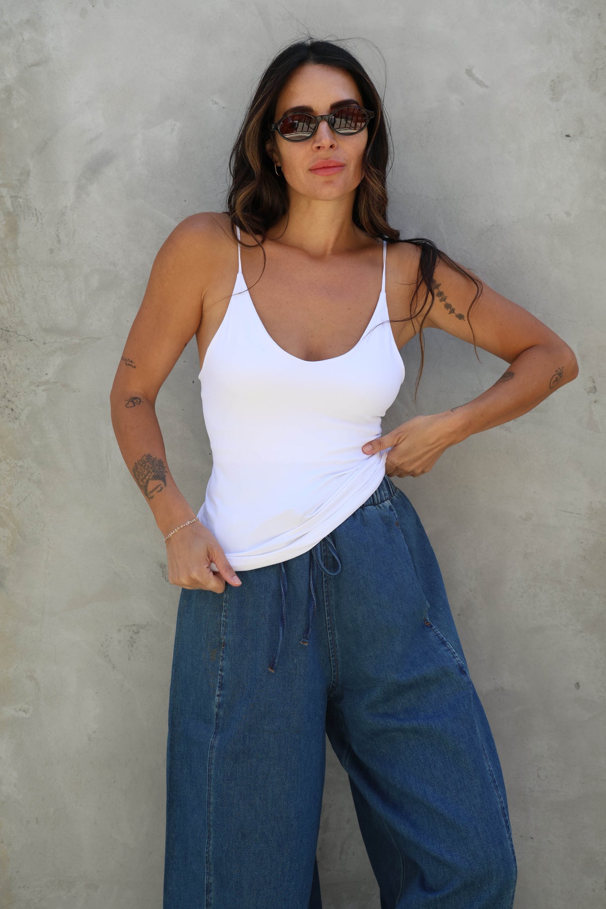 Woman wearing a white top and blue jeans against a gray wall