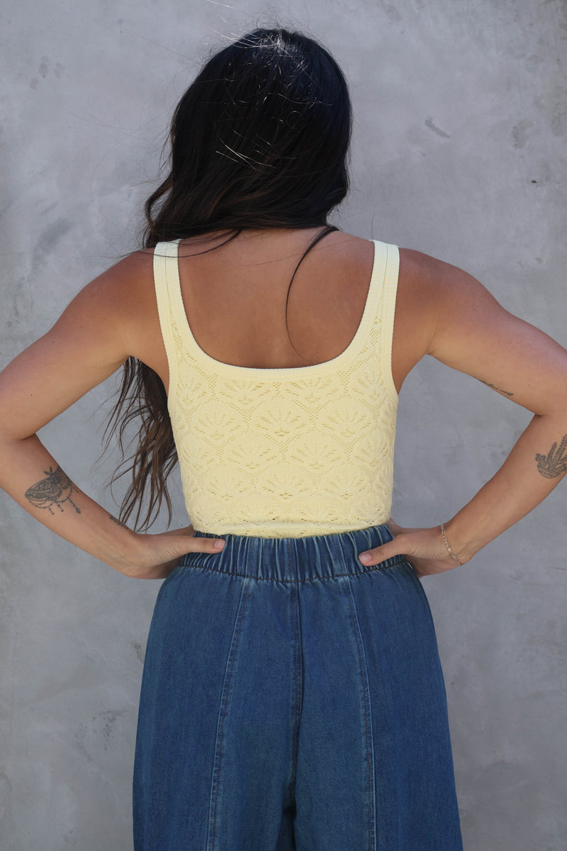 Person wearing a yellow top and blue pants against a gray wall