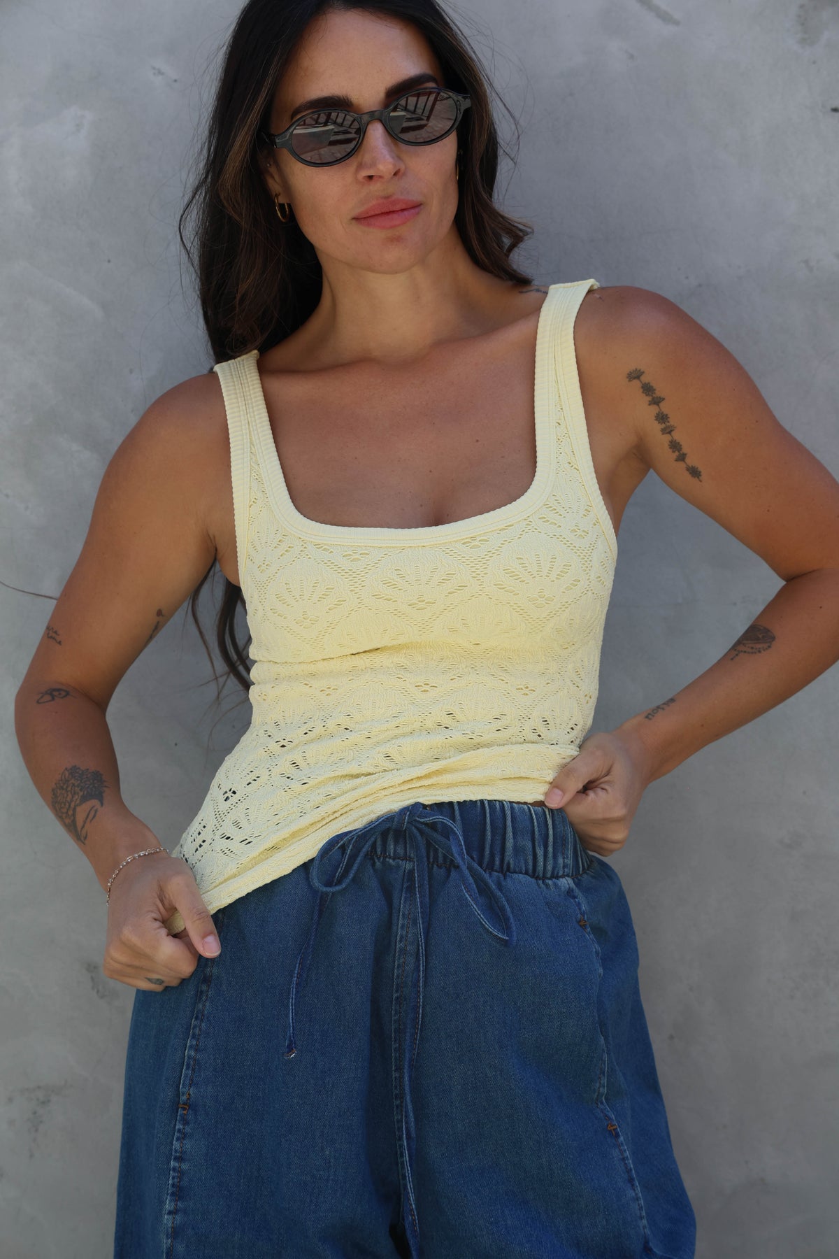 Woman wearing a yellow tank top and blue pants against a gray wall