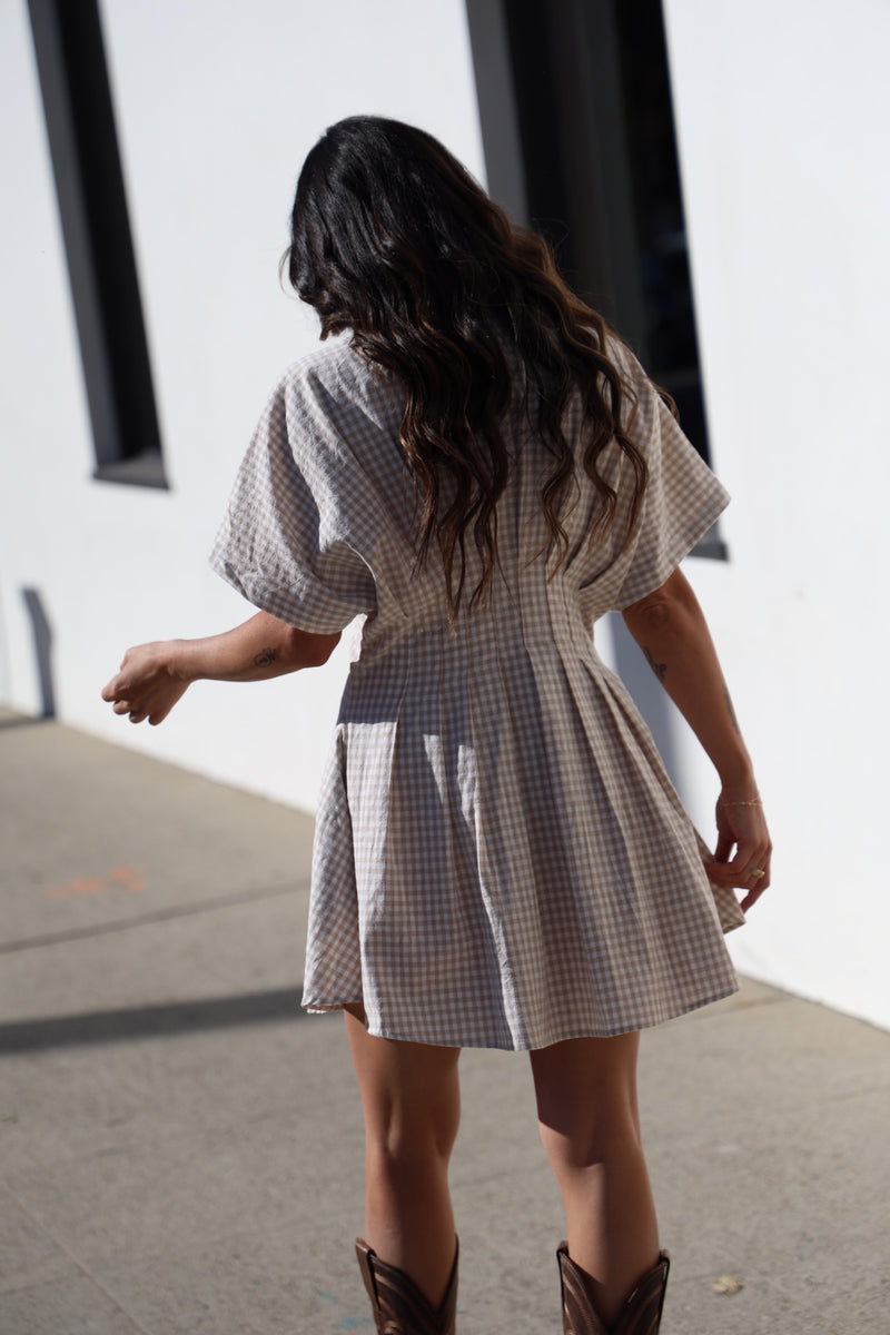 Person wearing a checkered dress and brown boots walking on a sidewalk.