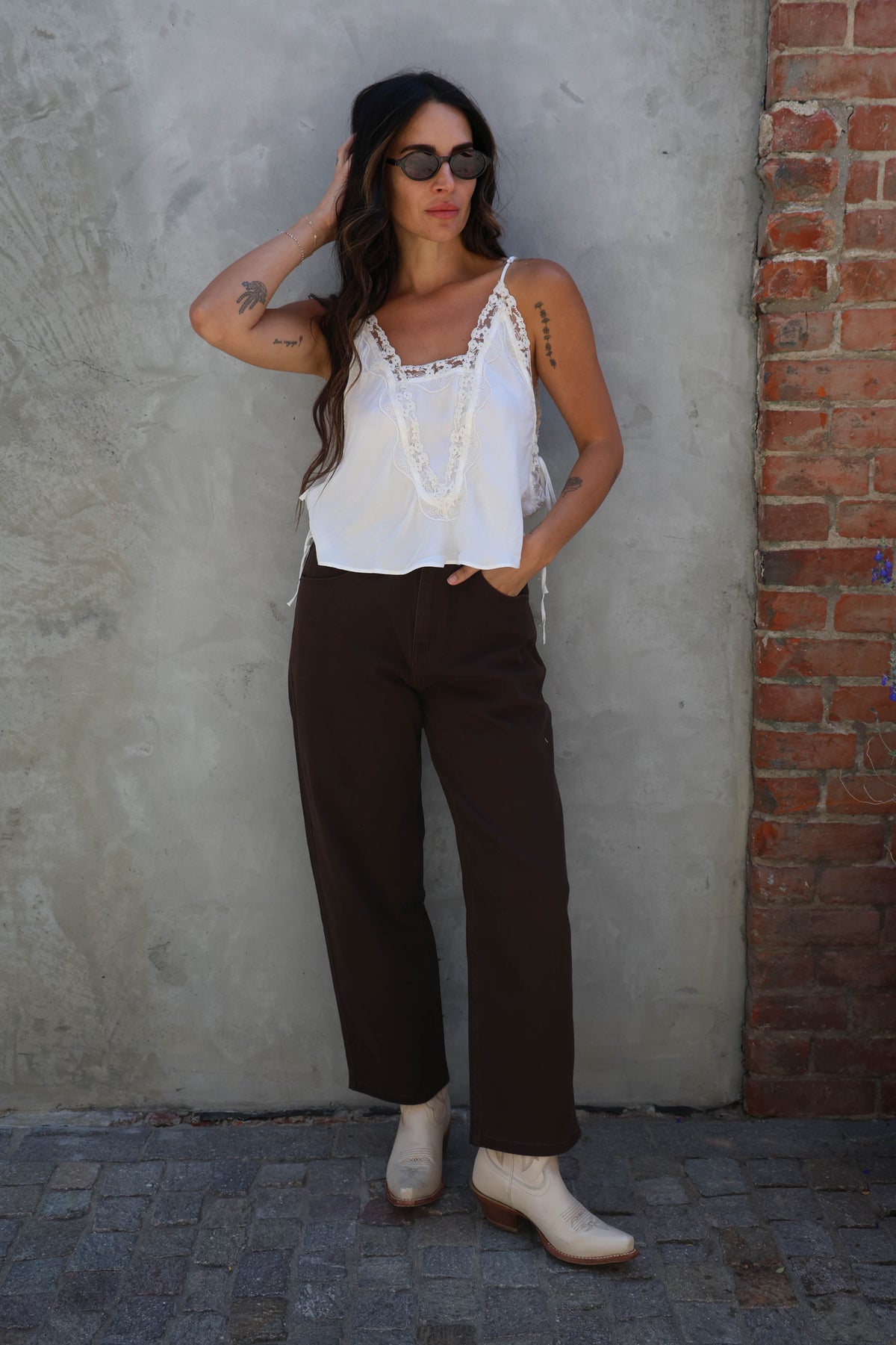 Woman wearing a white top and brown pants against a textured wall.