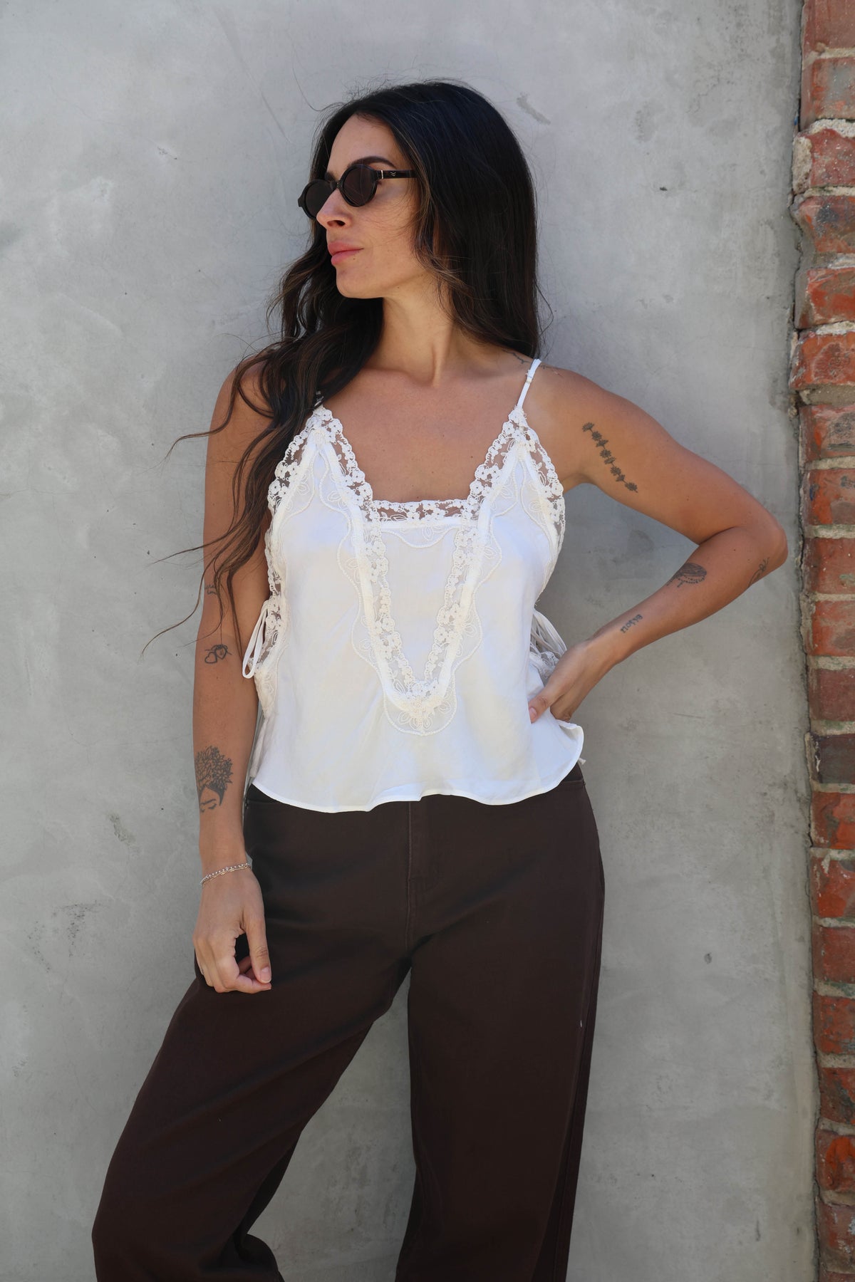 Woman wearing a white delicate lace tank in front of a grey wall