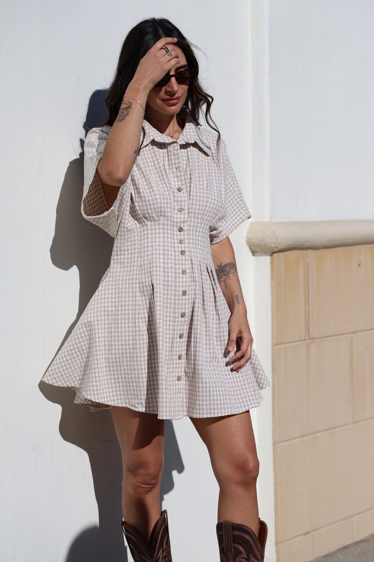 Woman wearing a checkered dress and brown boots against a white wall.