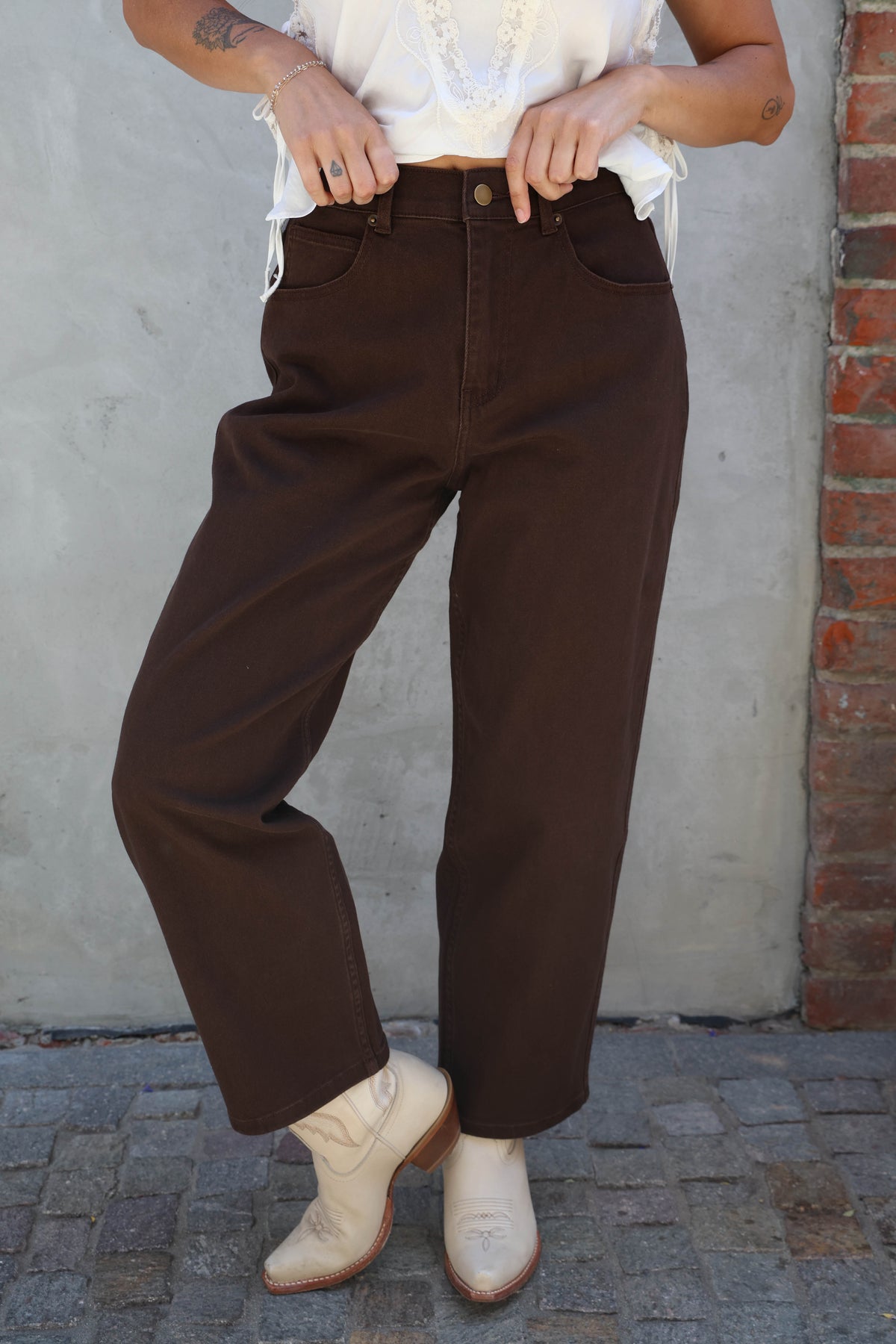 Person wearing brown pants and white blouse against a concrete wall.