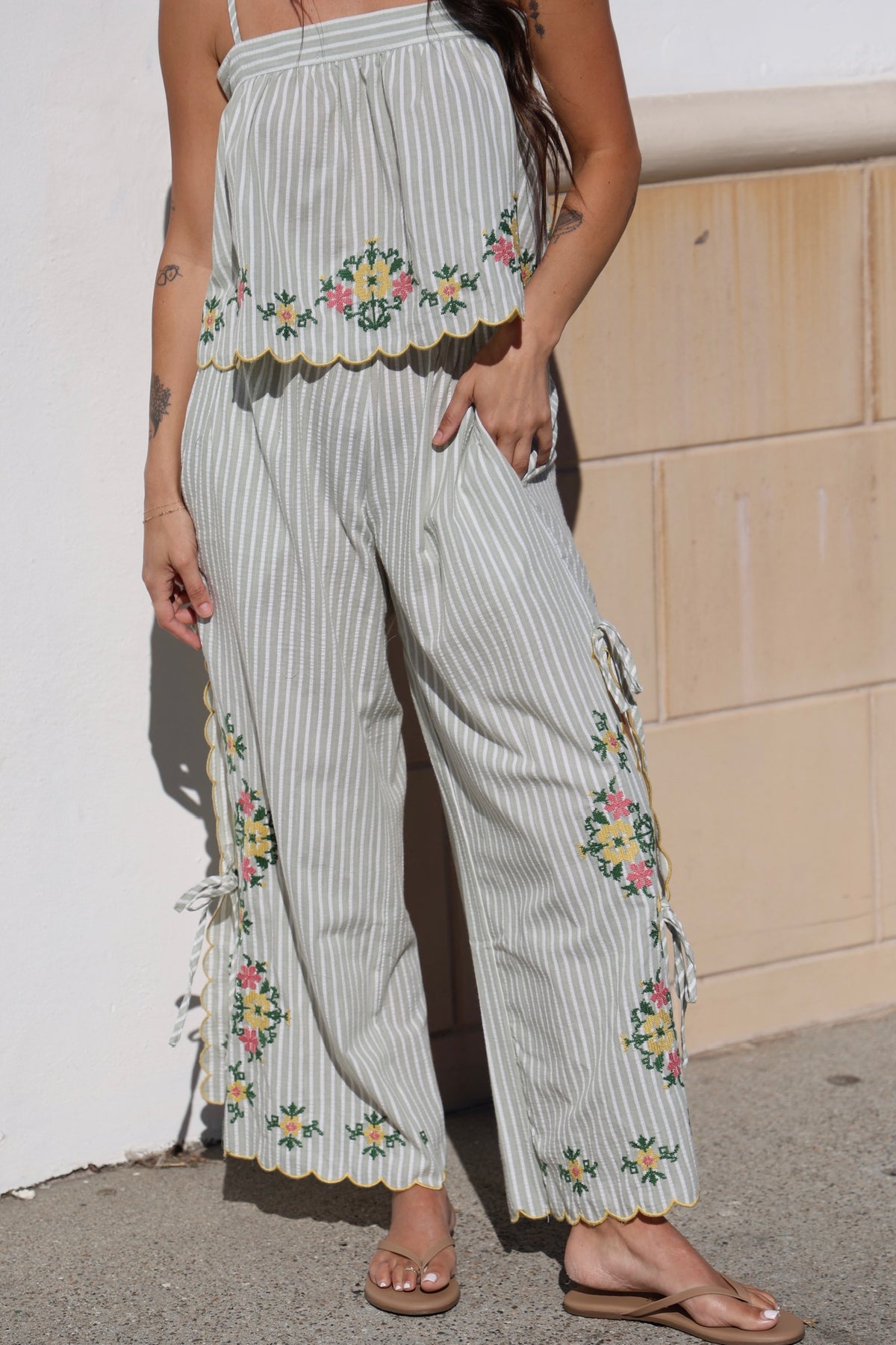 Woman wearing a light-colored outfit with floral embroidery against a white wall.