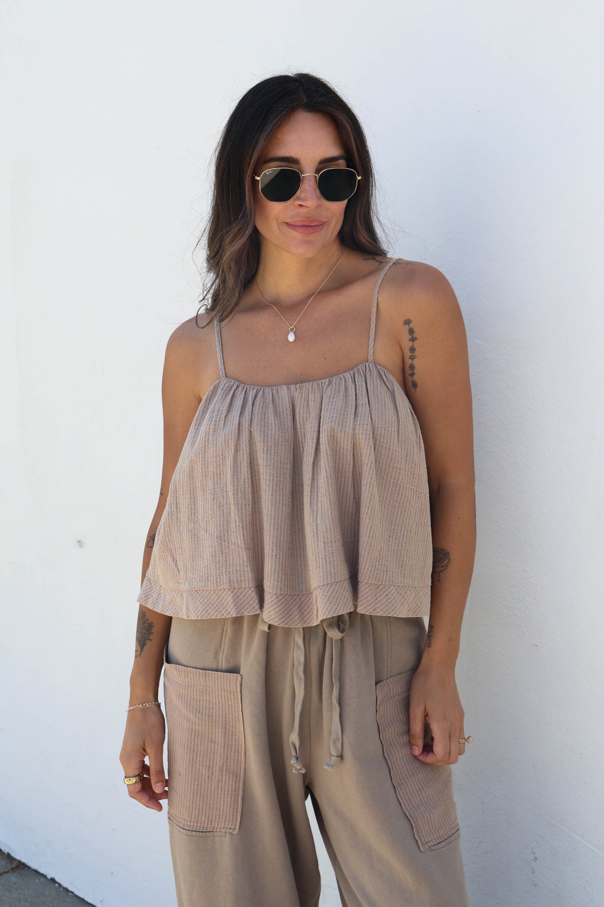 A woman modeling a two-piece lounge set consisting of a beige ribbed crinkle camisole top and matching corduroy cargo pants, set against a plain white wall.