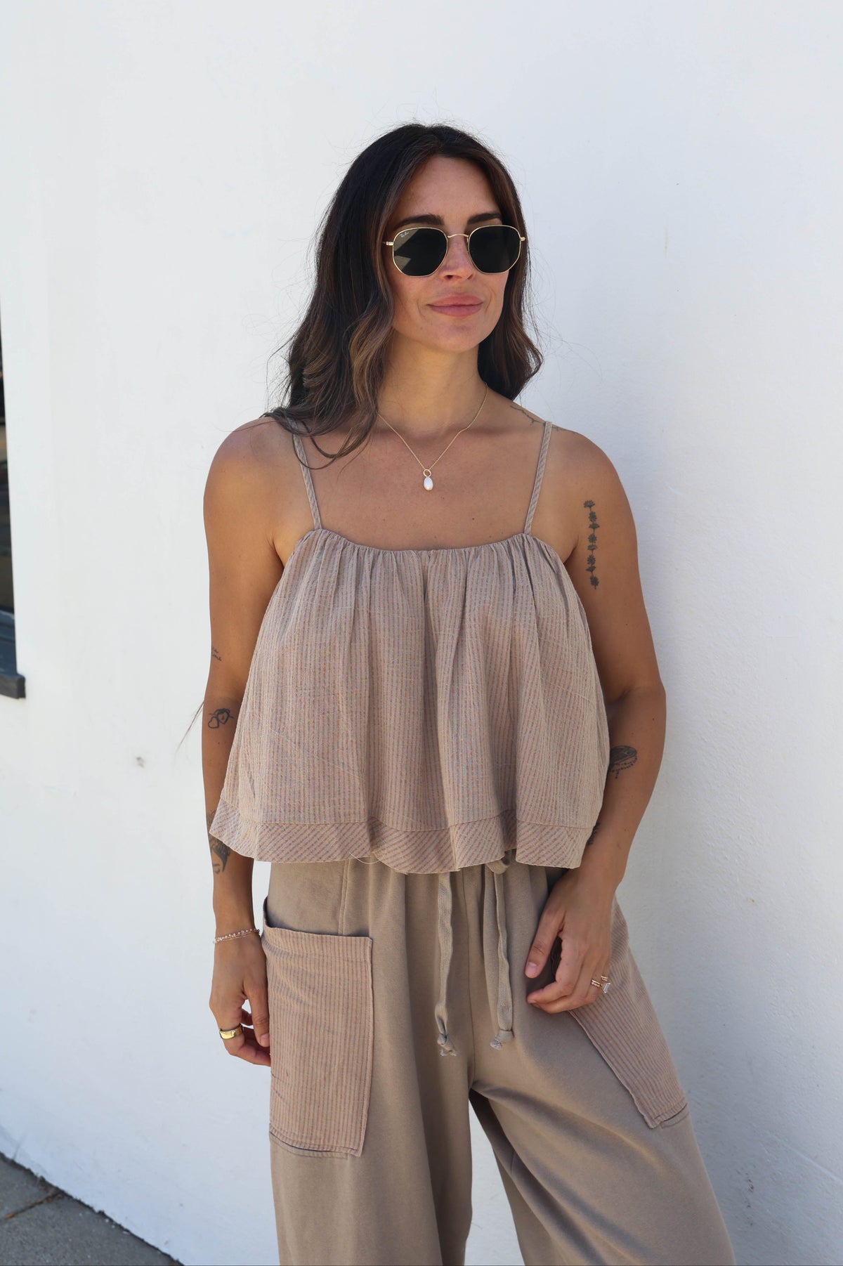 A woman wearing a beige ribbed camisole top with thin straps and matching wide-leg cargo pants, standing against a plain white wall.