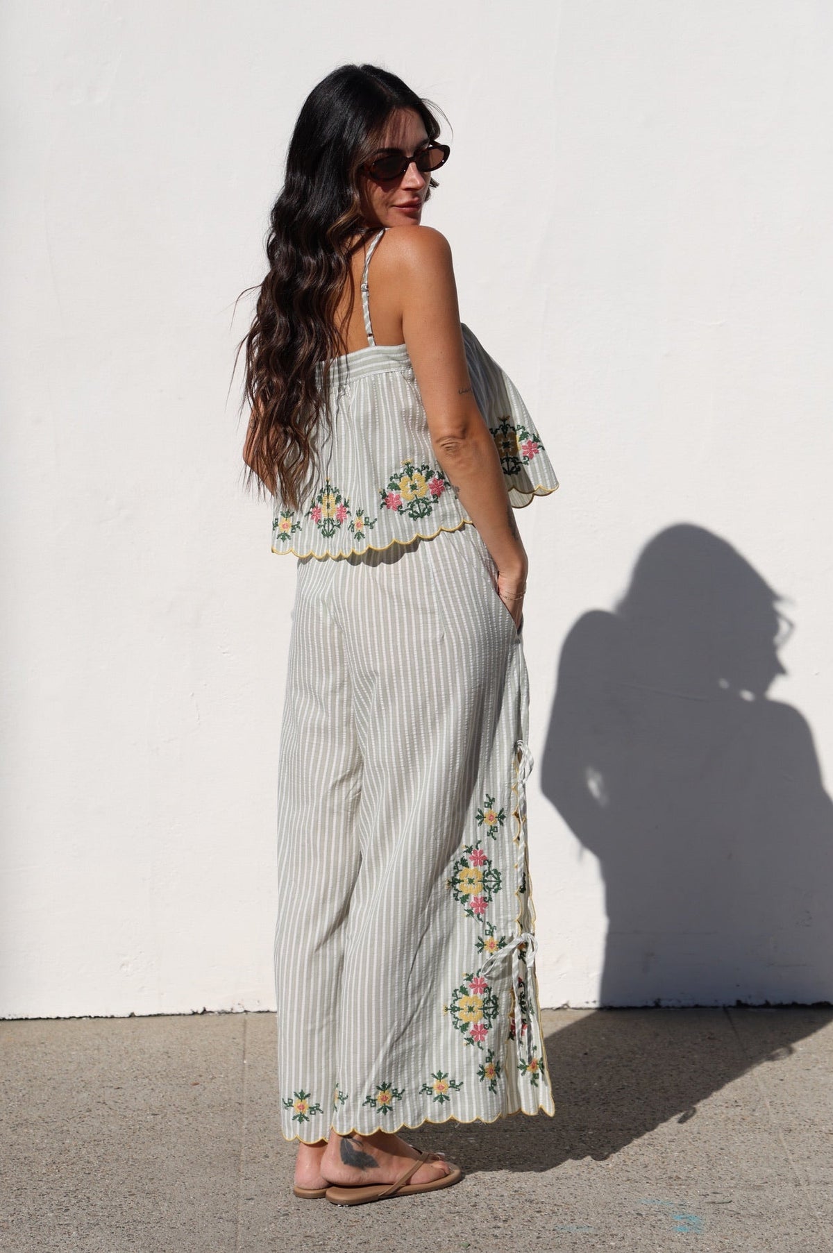 Woman wearing a floral dress standing against a white wall.