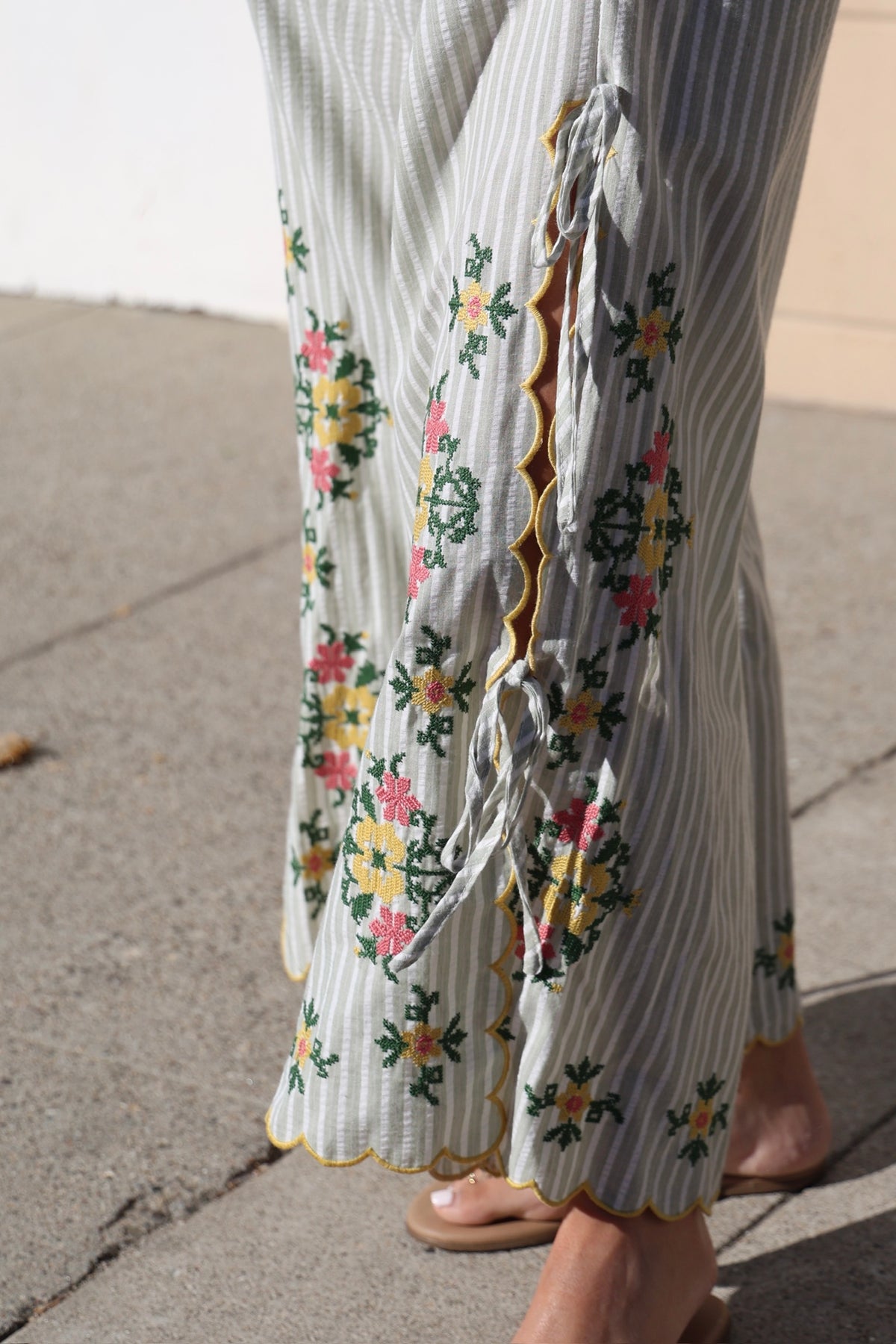 Close-up of a person wearing a floral dress with a striped pattern on a sidewalk.