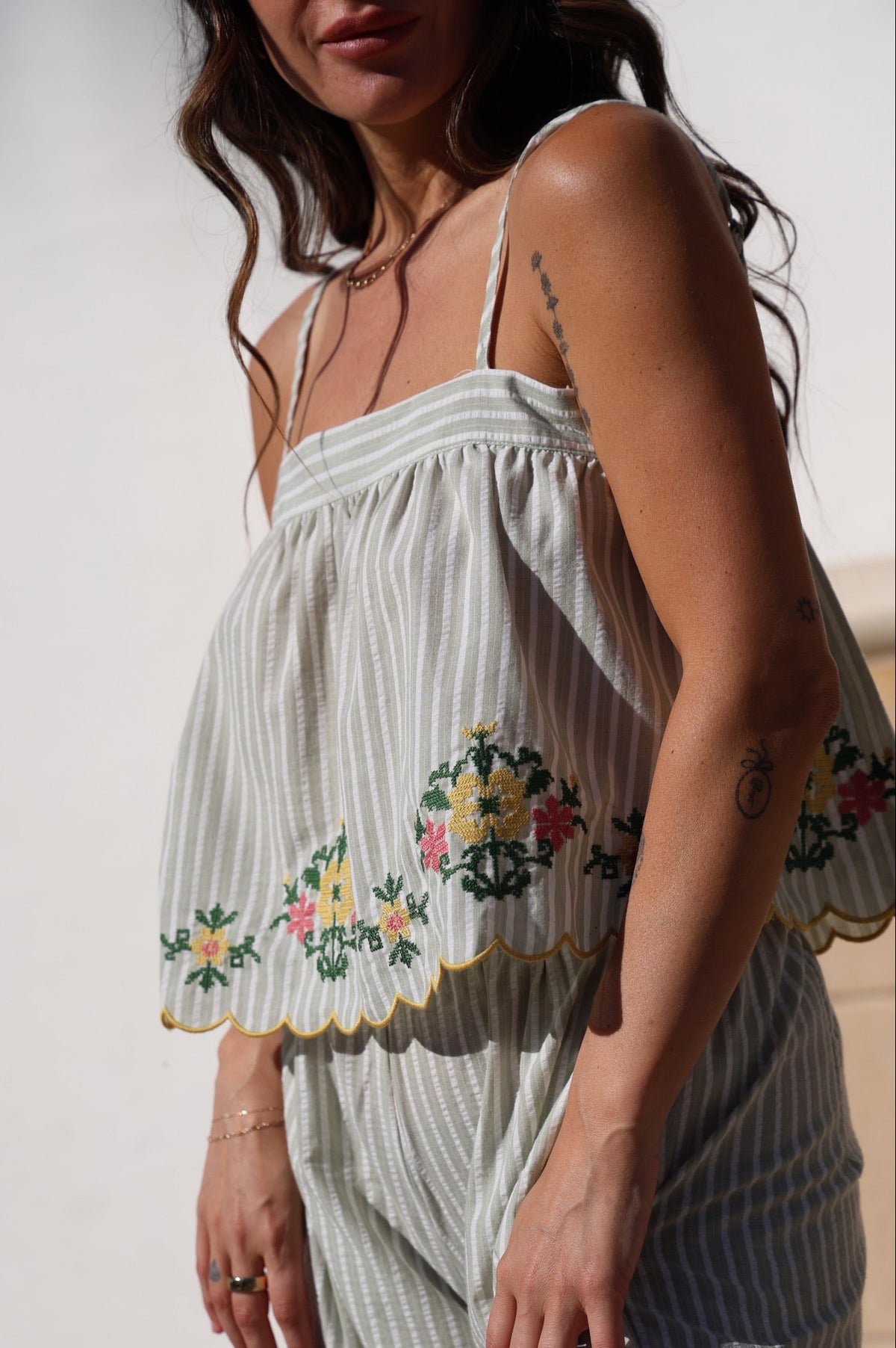 Woman wearing a light-colored dress with floral embroidery against a neutral background