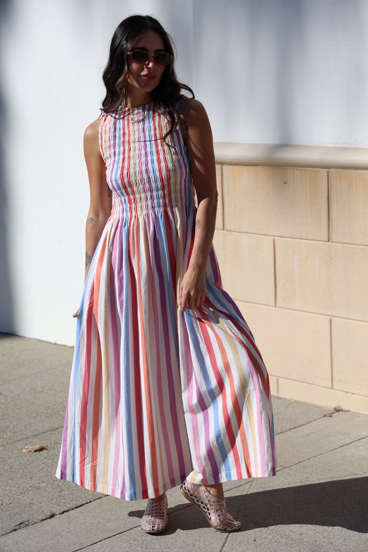 Woman wearing a colorful striped dress standing on a sidewalk.
