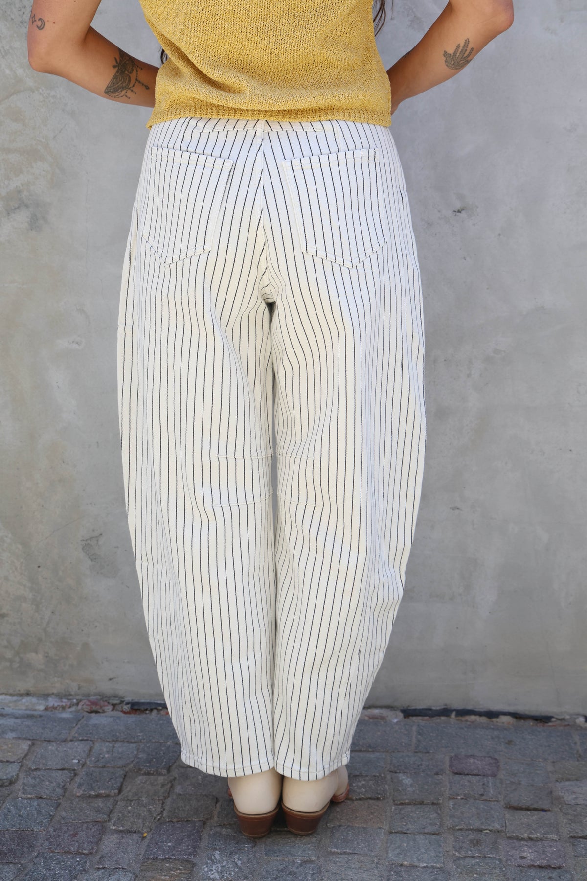 Person wearing a yellow top and white striped pants against a gray wall.