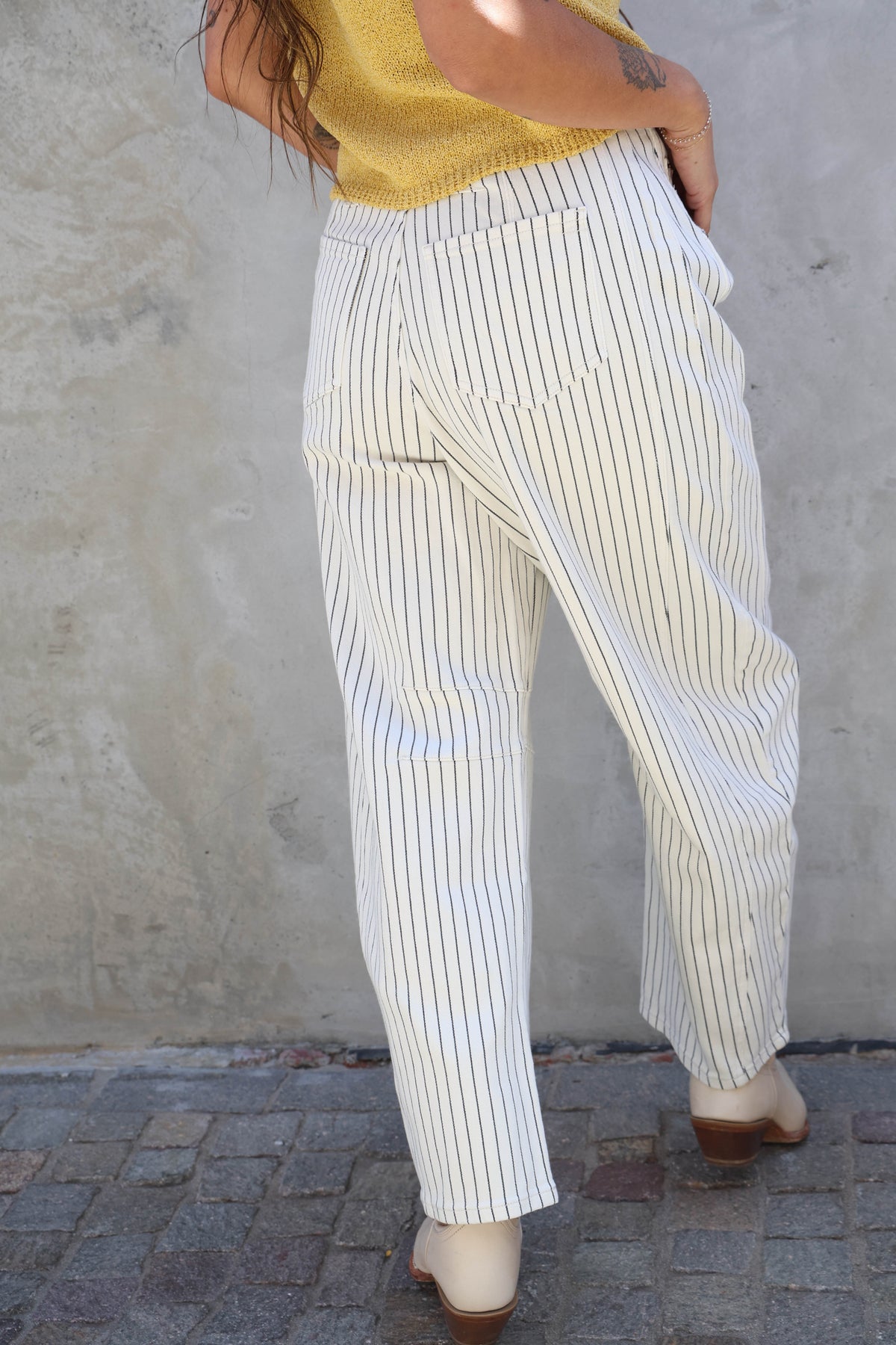 Person wearing white and gray striped pants against a plain wall.