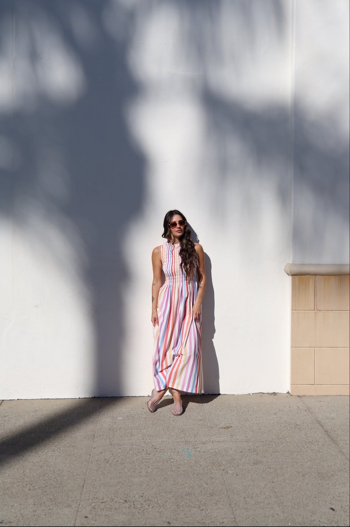 Woman in a striped dress standing against a white wall with shadows.