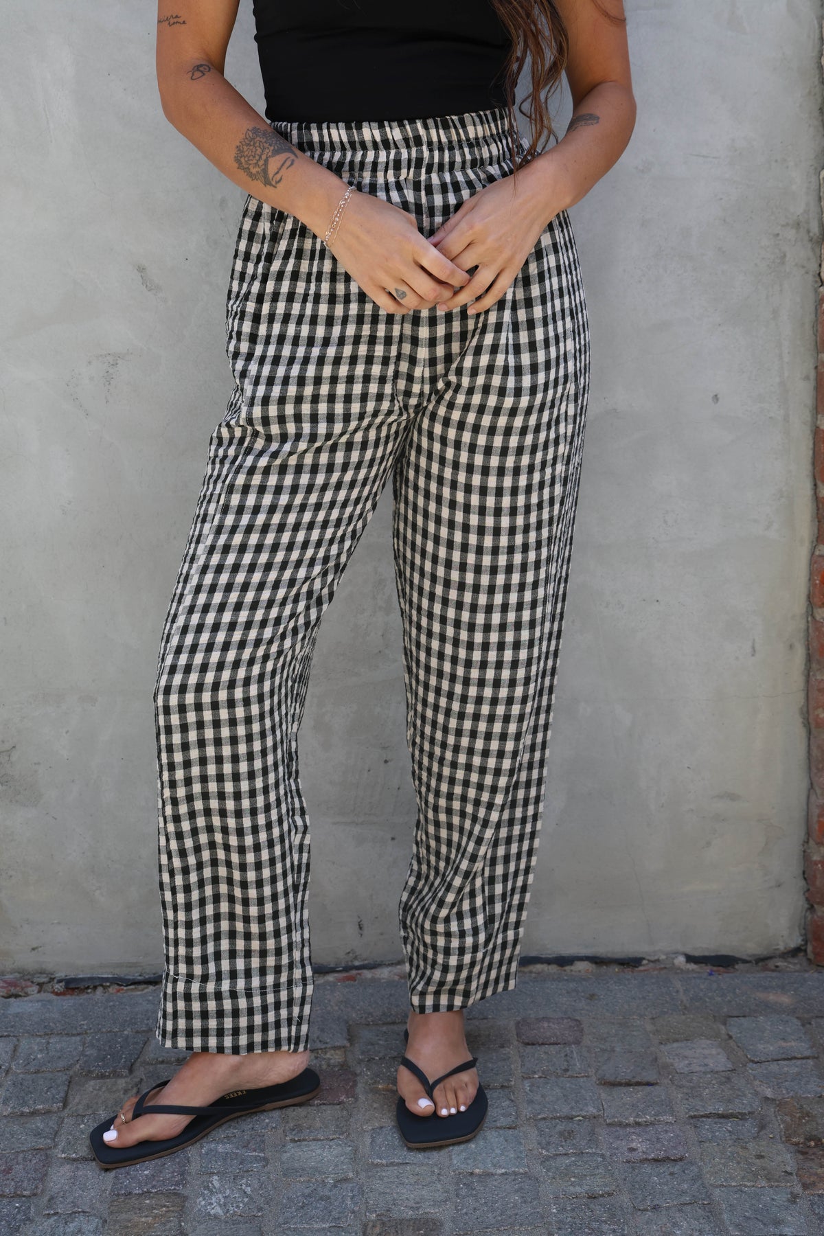 Person wearing black and white checkered pants standing against a plain wall.