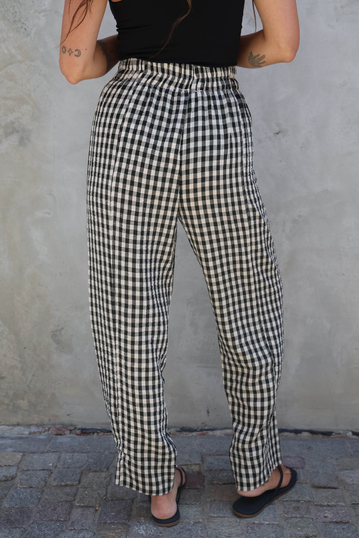 Person wearing black and white checkered pants against a plain wall.