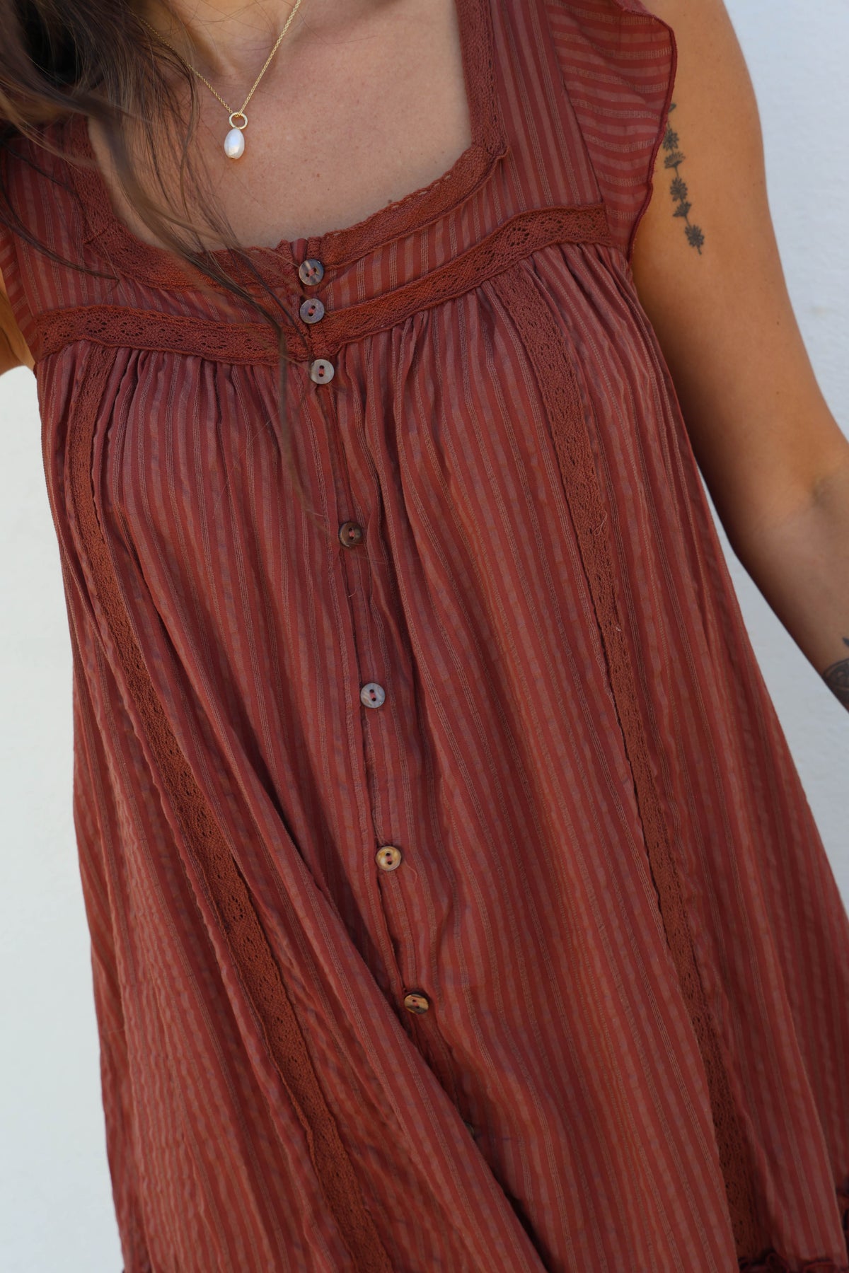 A close-up of a woman wearing a rust-colored sleeveless top or dress with vertical textured stripes, a button-down front, and a square neckline.