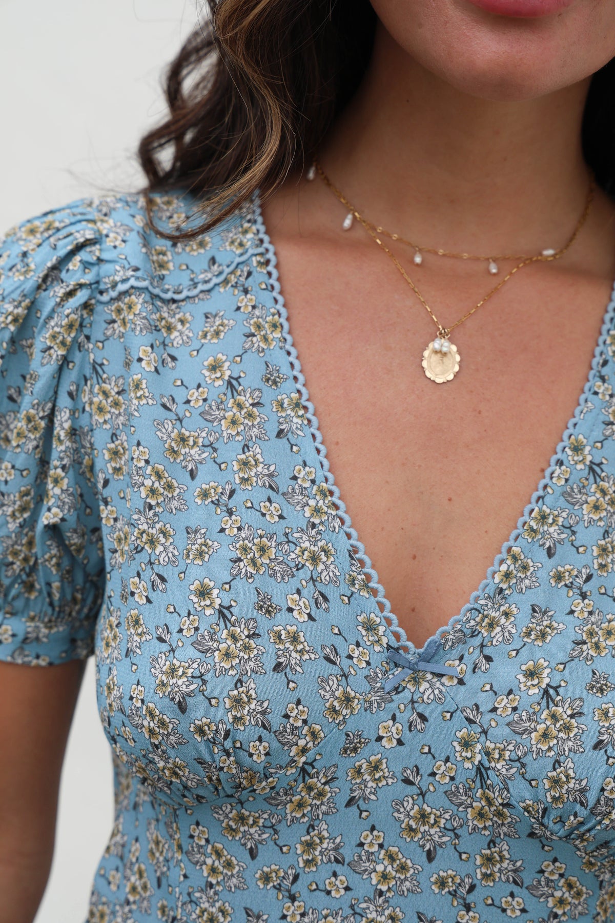 Close-up of a person wearing a blue floral dress with a necklace.