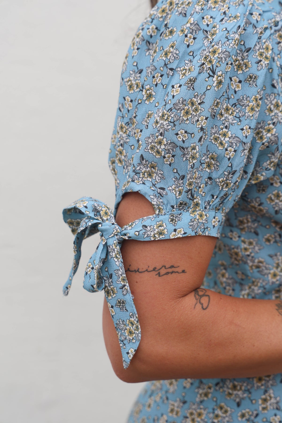 Person wearing a blue floral dress with a tie detail on a plain background