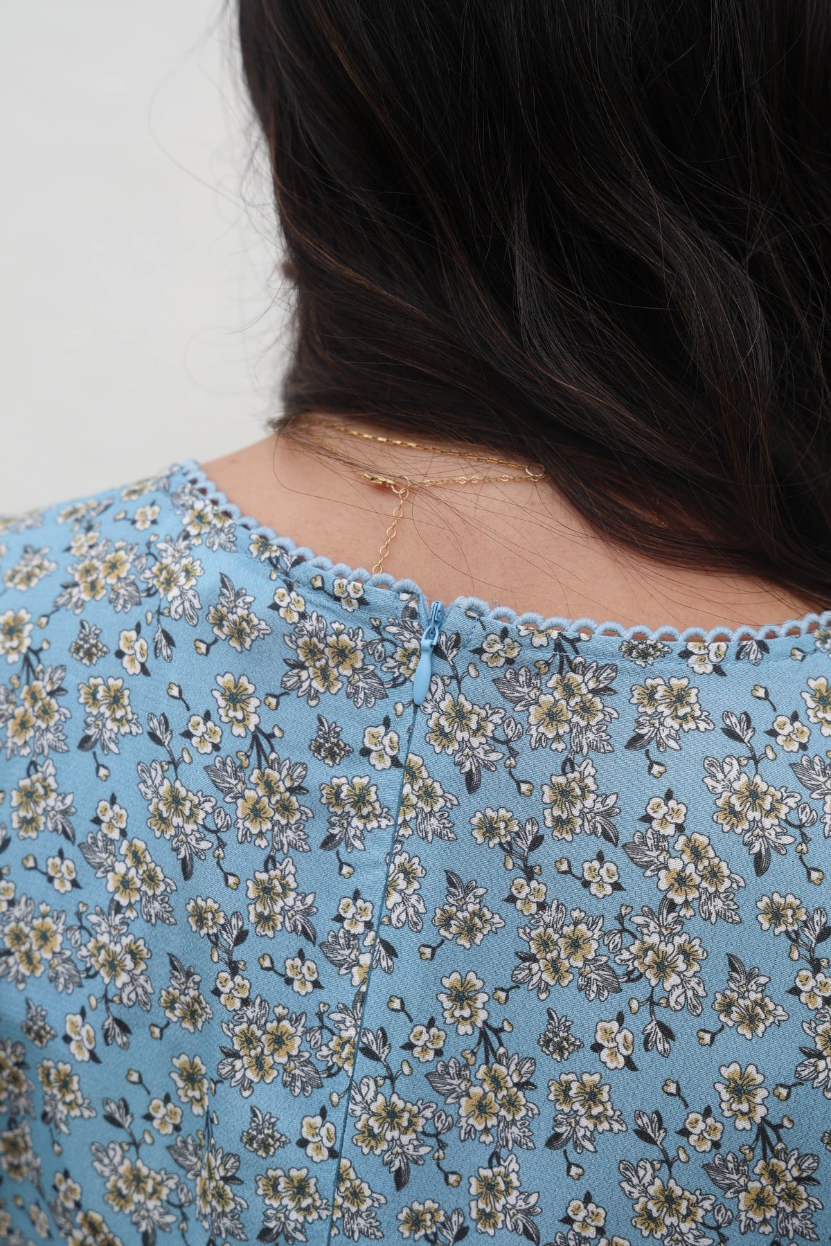 Close-up of a person wearing a blue floral dress with a plain background