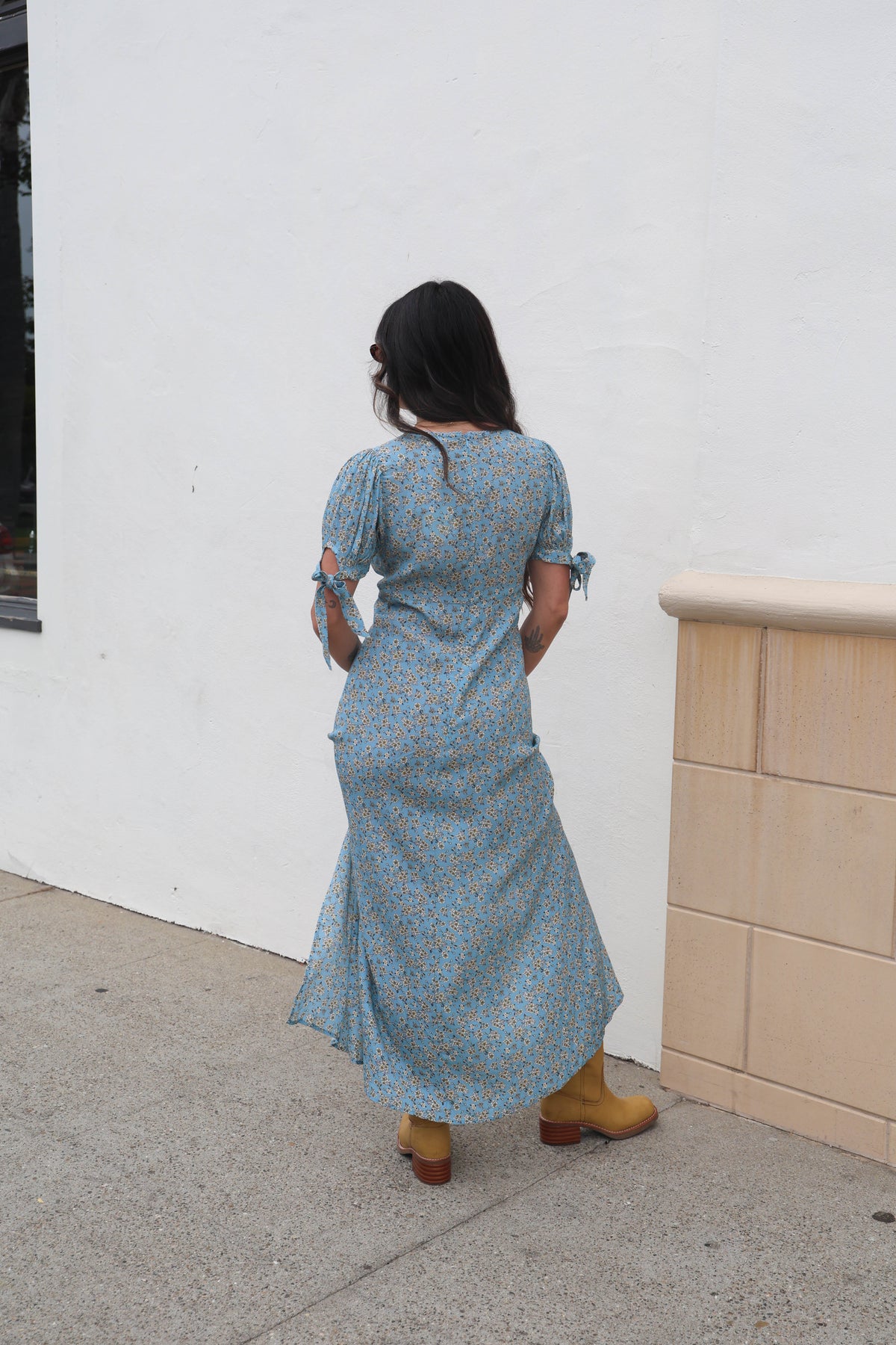 Woman in a blue dress standing against a white wall with a beige cabinet.