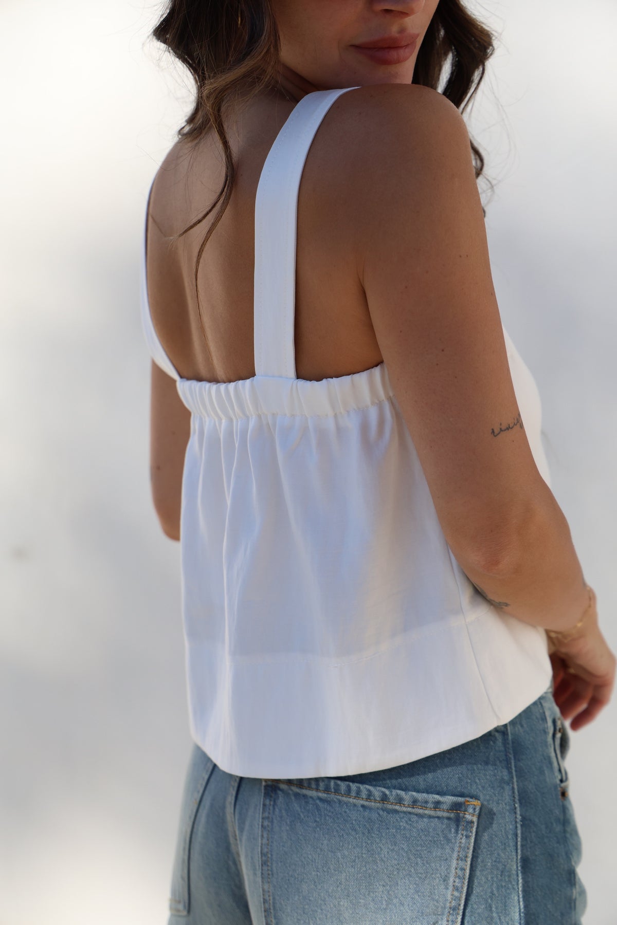 Woman wearing a white sleeveless top and blue jeans against a white background