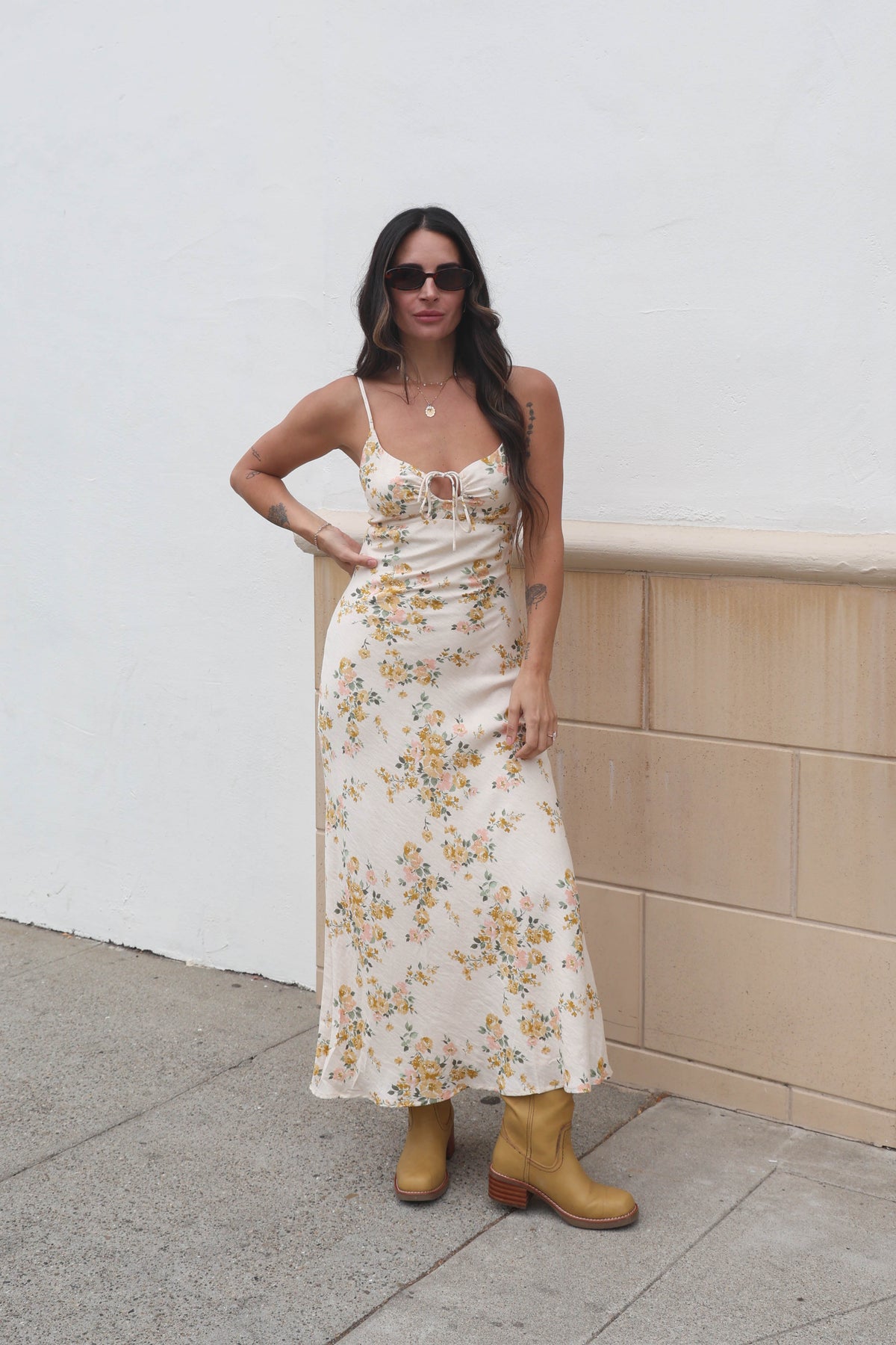 Woman in a floral dress standing against a white wall.