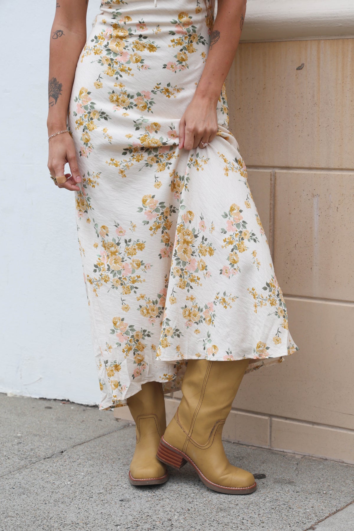 Person wearing a floral dress and yellow boots against a white wall.