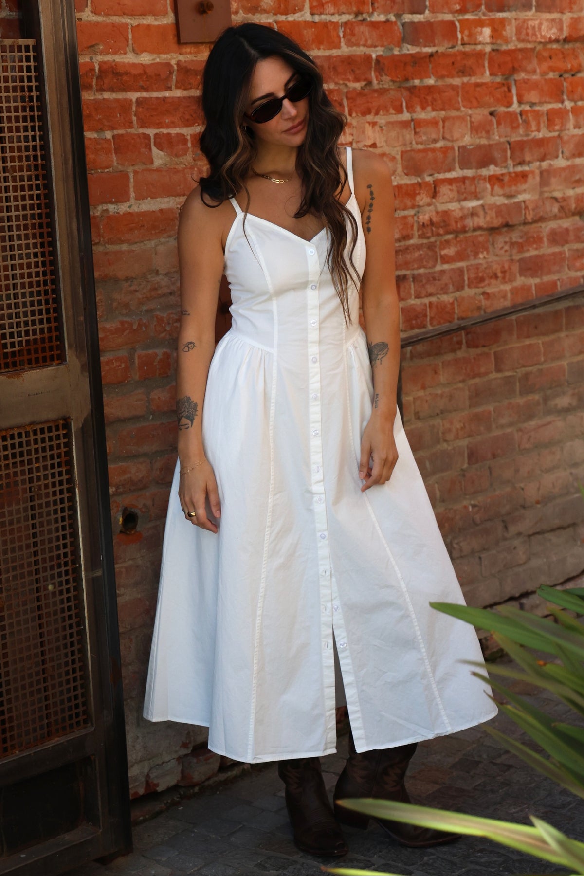 Woman wearing a white dress standing against a brick wall.