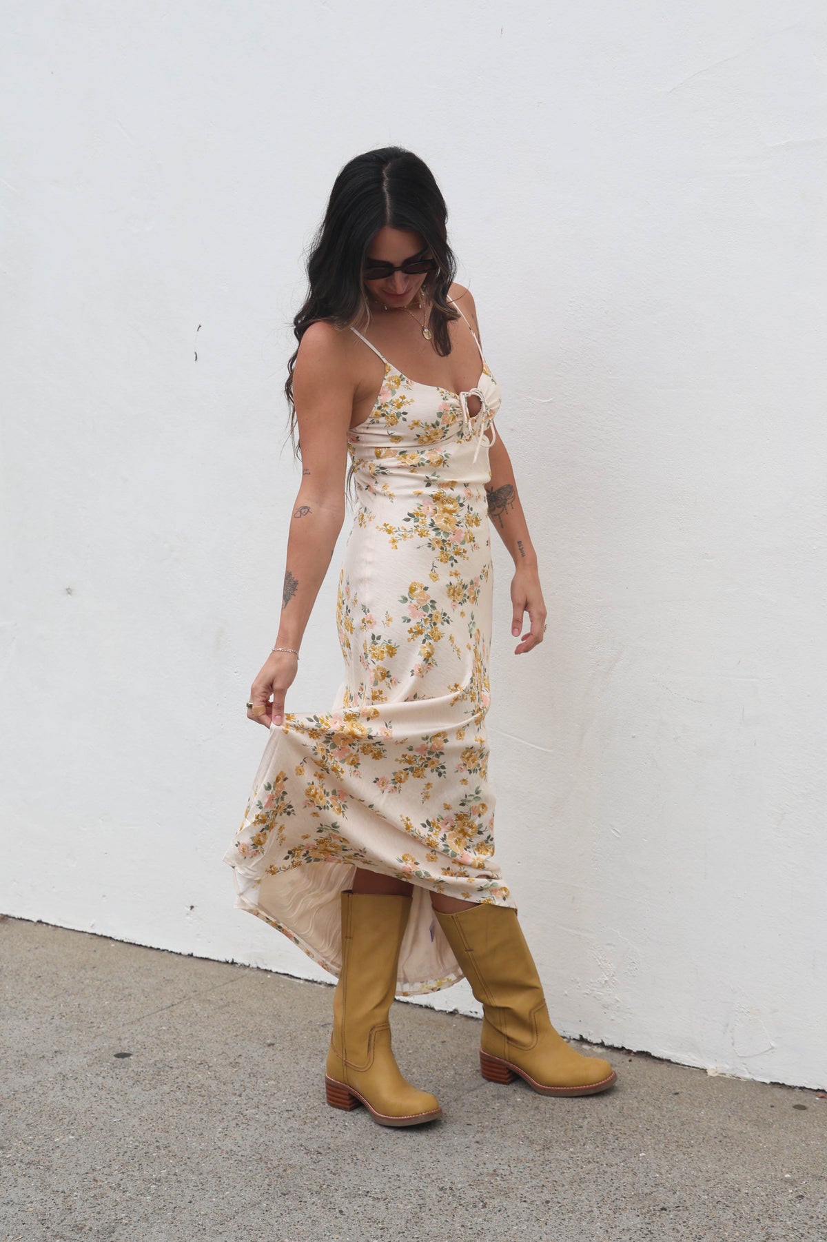Woman wearing a floral dress and yellow boots against a white wall.