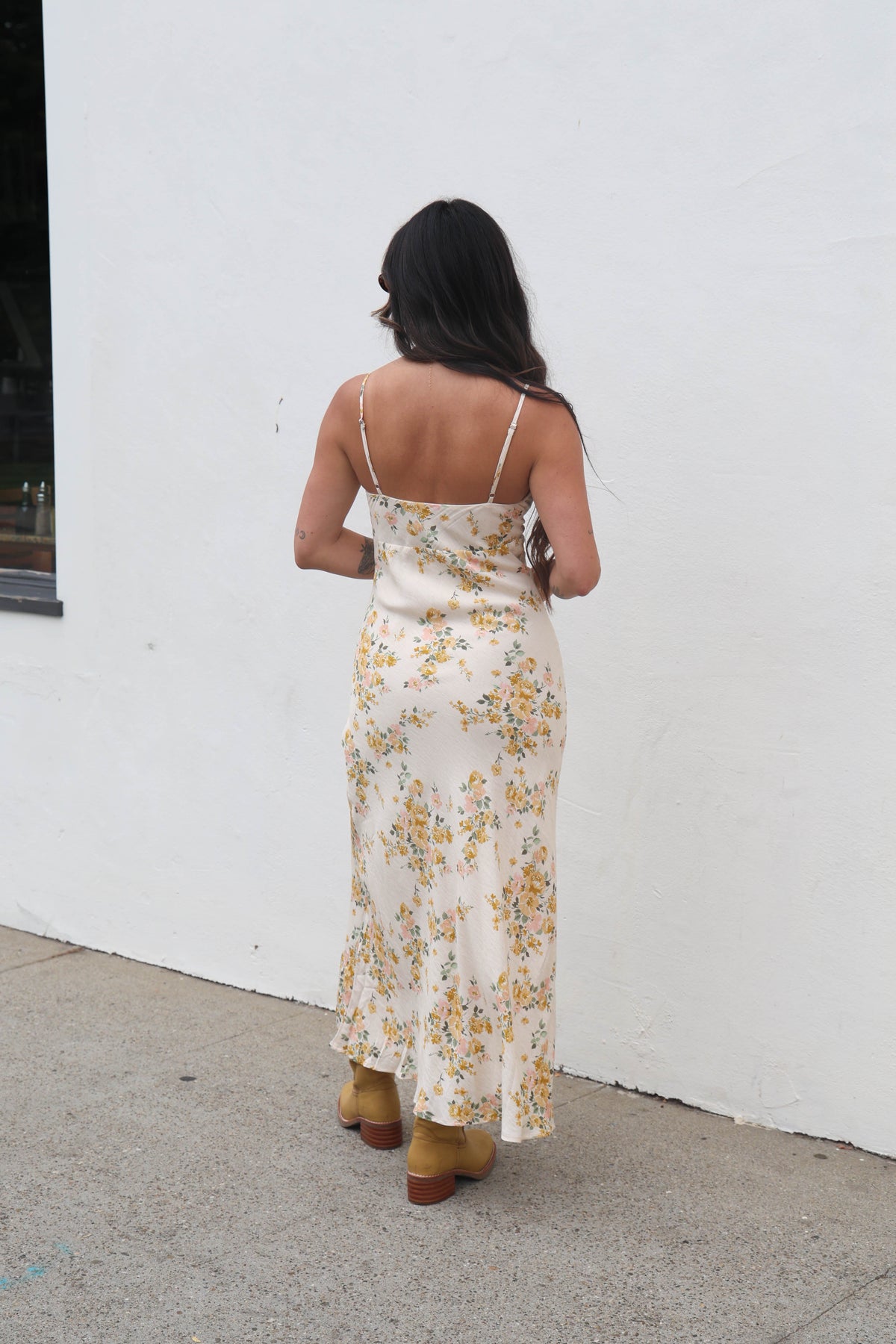 Woman wearing a floral dress standing against a white wall.