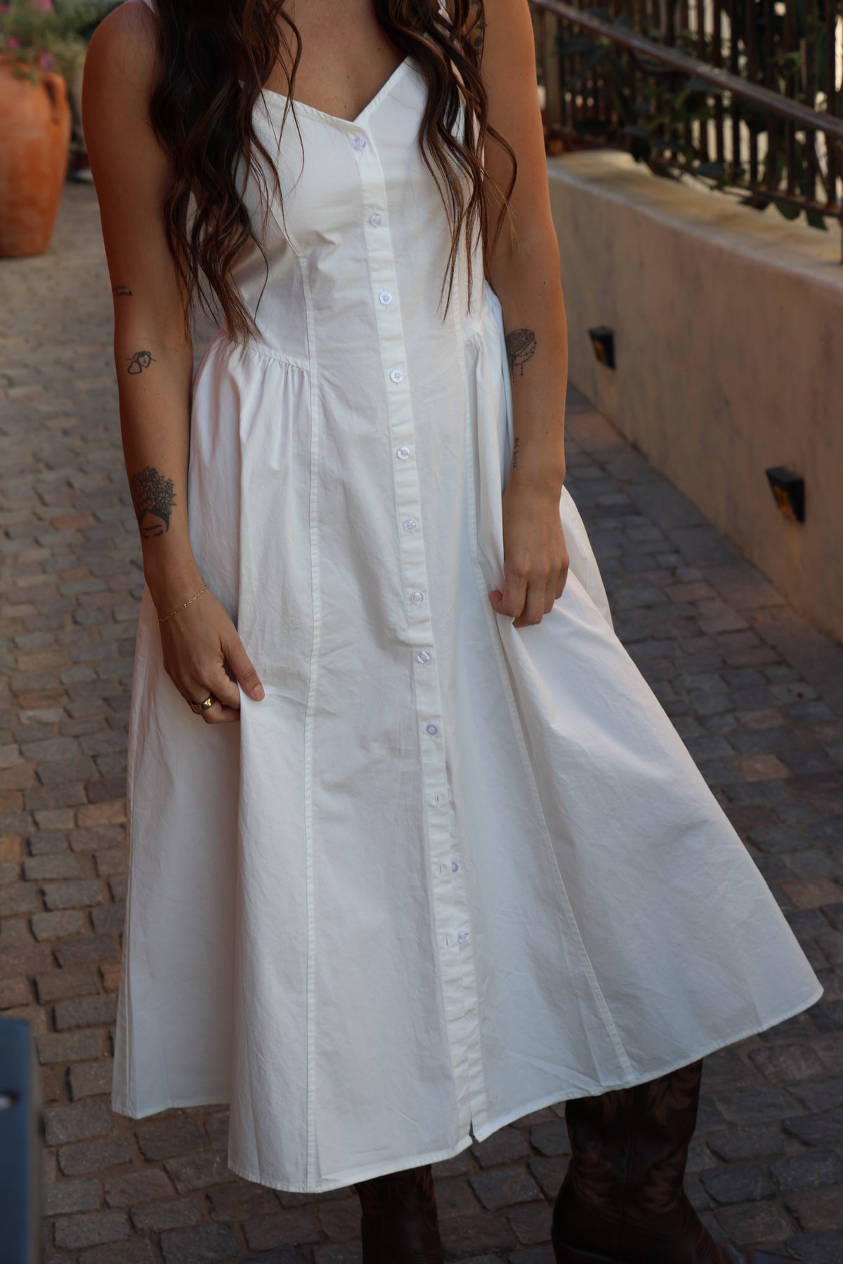 Woman wearing a white dress standing on a brick pavement.