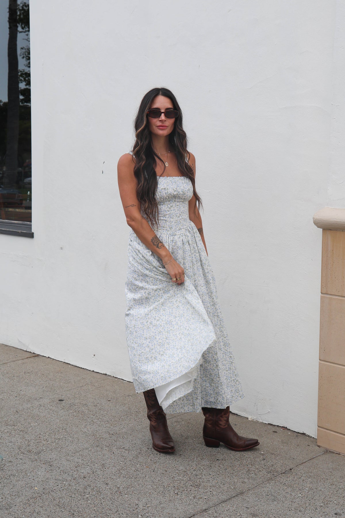 Woman in a white dress and brown boots standing against a white wall.