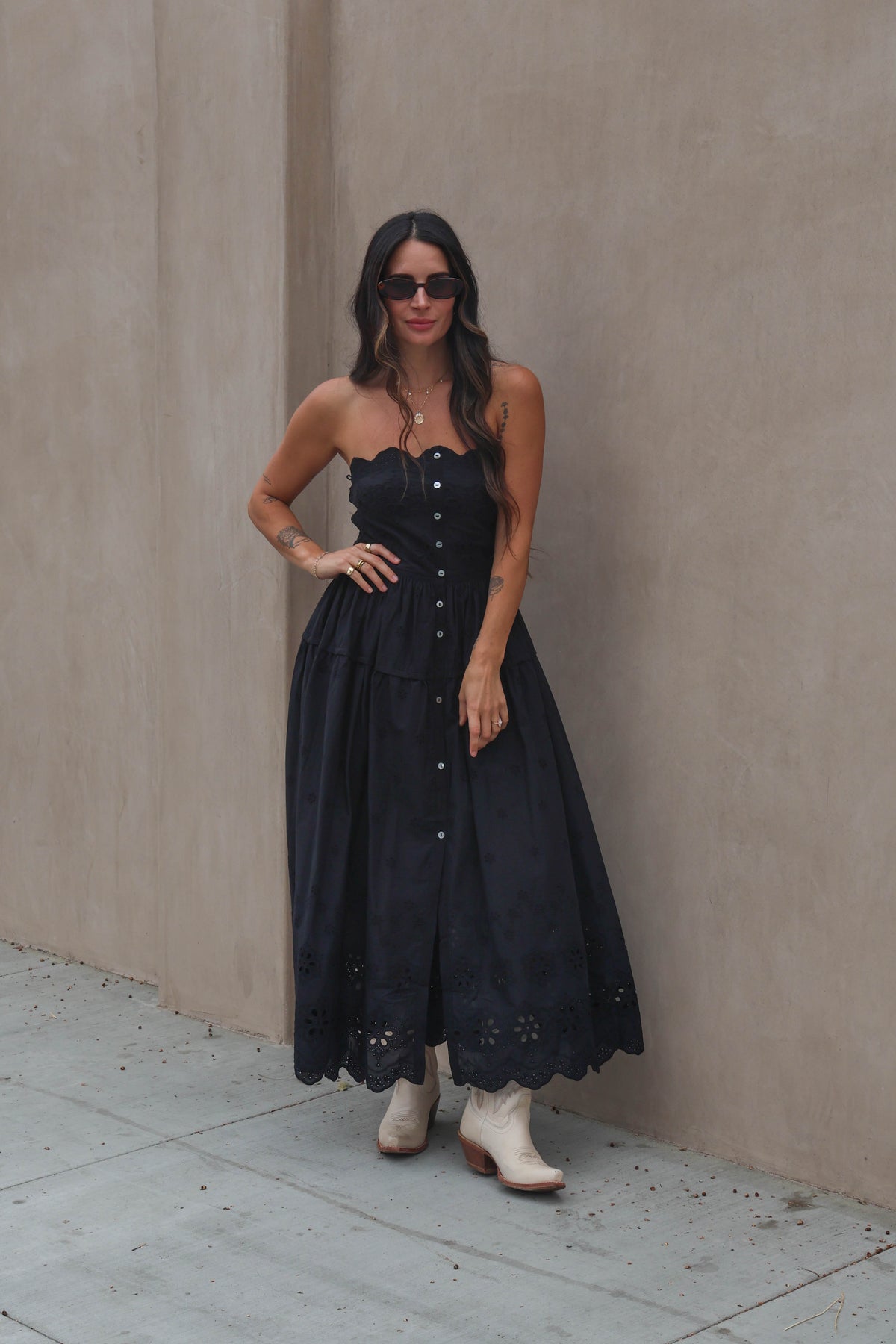 Woman wearing a black dress and white boots against a beige wall.