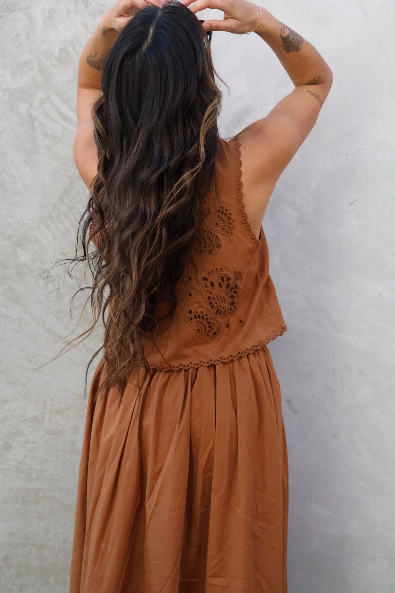 Woman wearing a brown sleeveless dress with intricate back design against a plain background