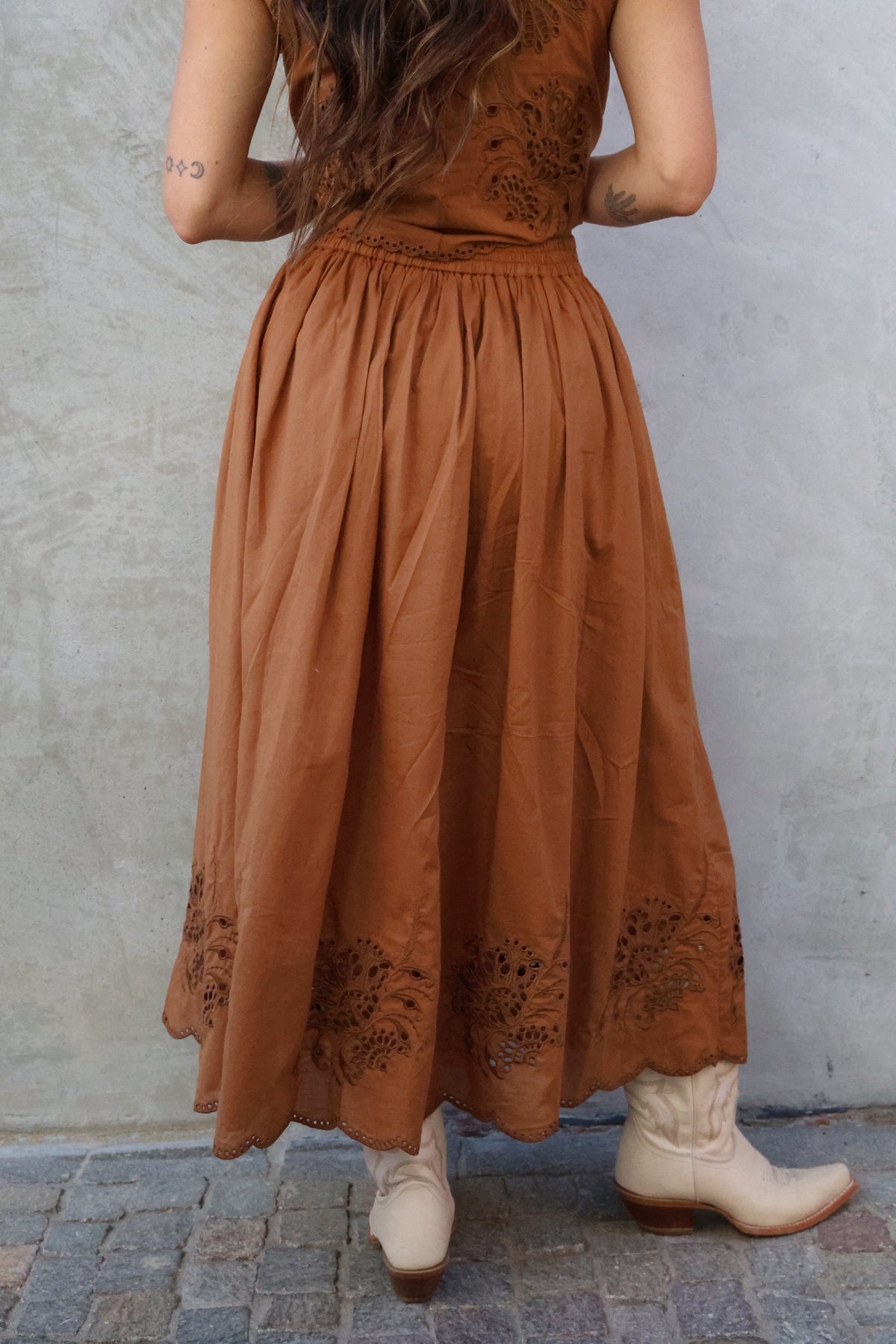 Person wearing a long brown dress with lace details on a stone pavement.