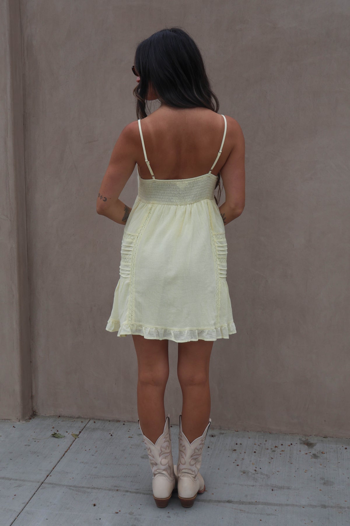 Woman wearing a light green dress and white boots against a plain wall.