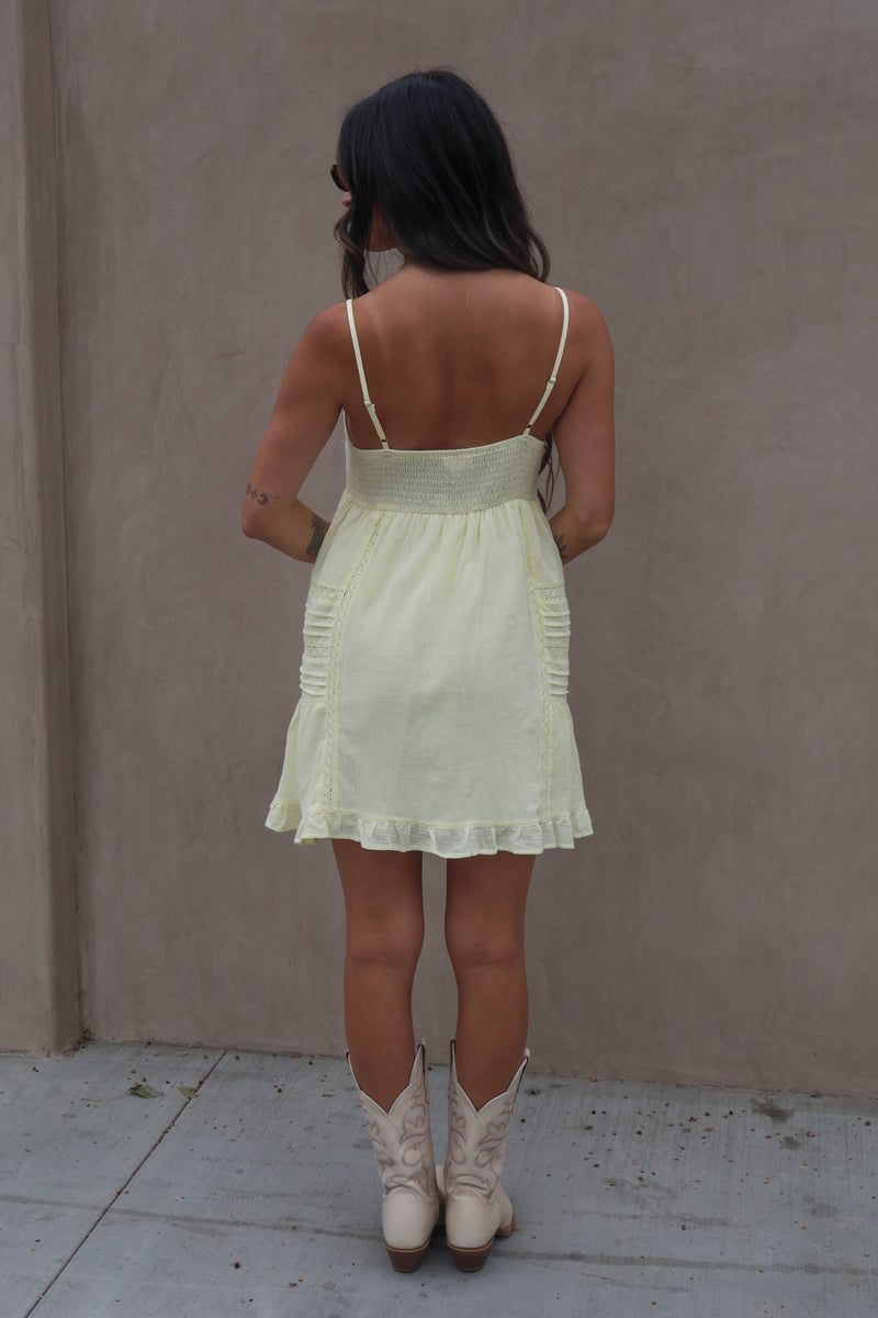 Woman wearing a light green dress and white boots against a plain wall.