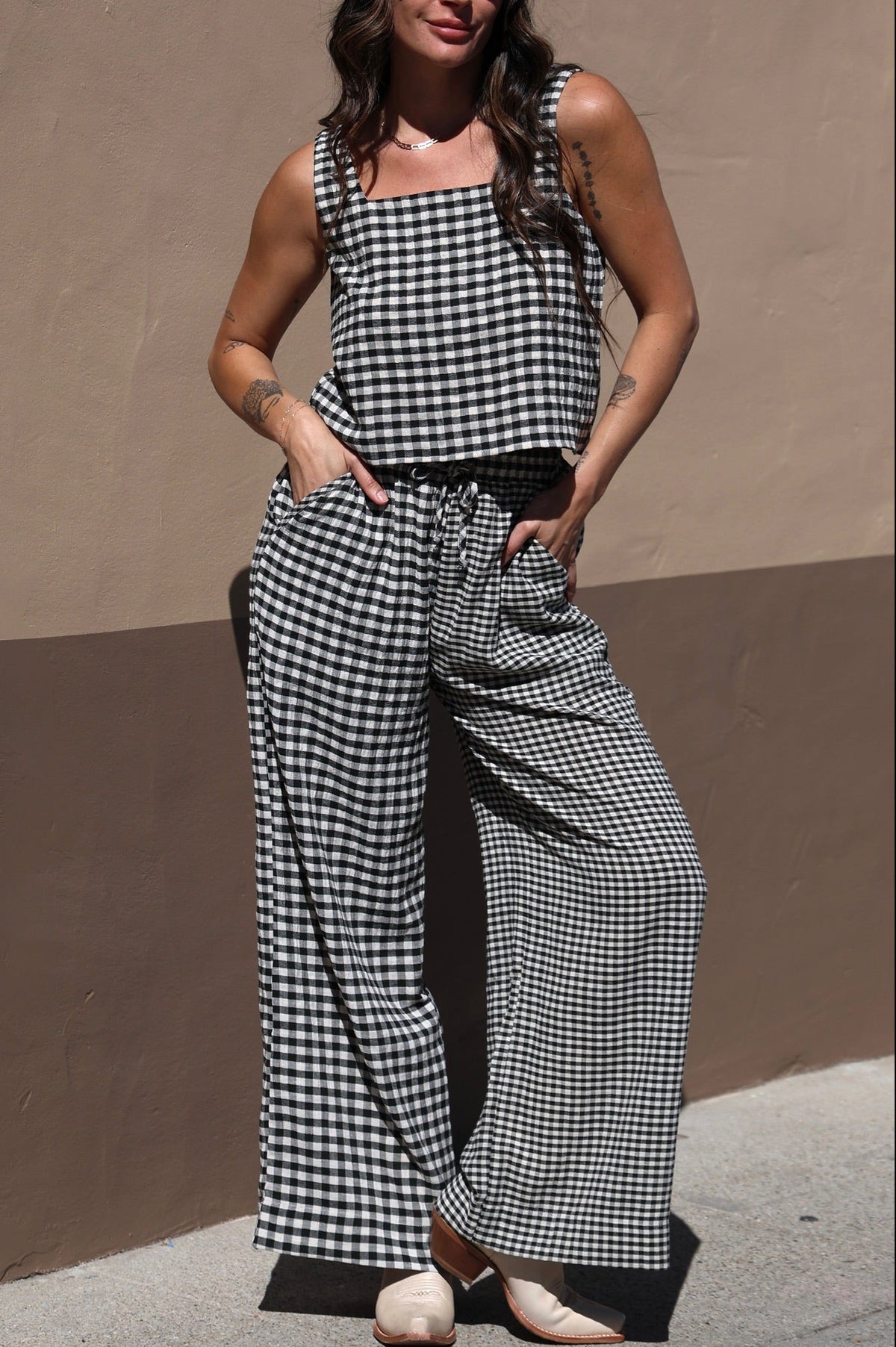 Woman wearing a black and white checkered outfit against a beige wall.