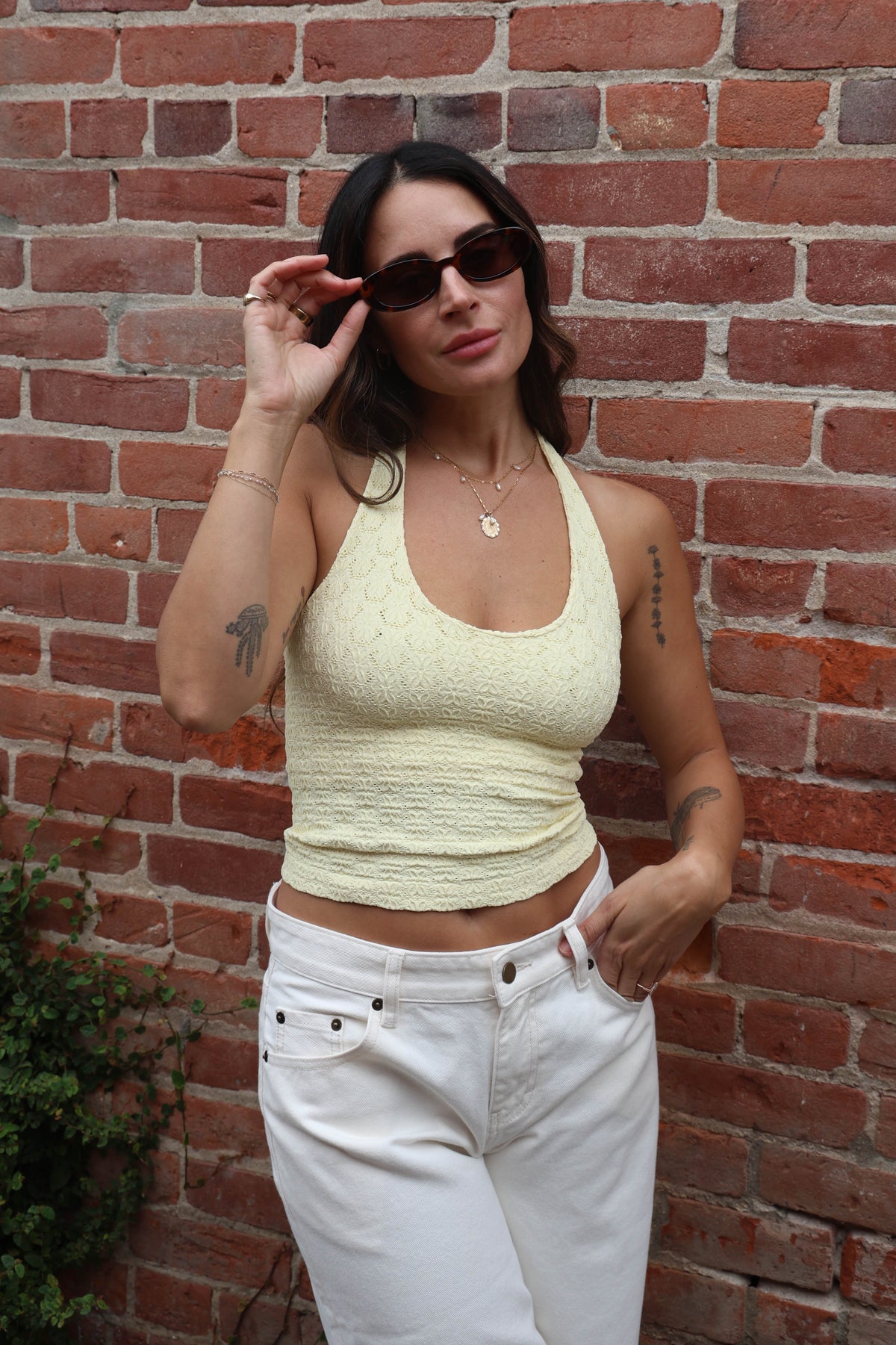Woman wearing a yellow top and white pants against a brick wall.