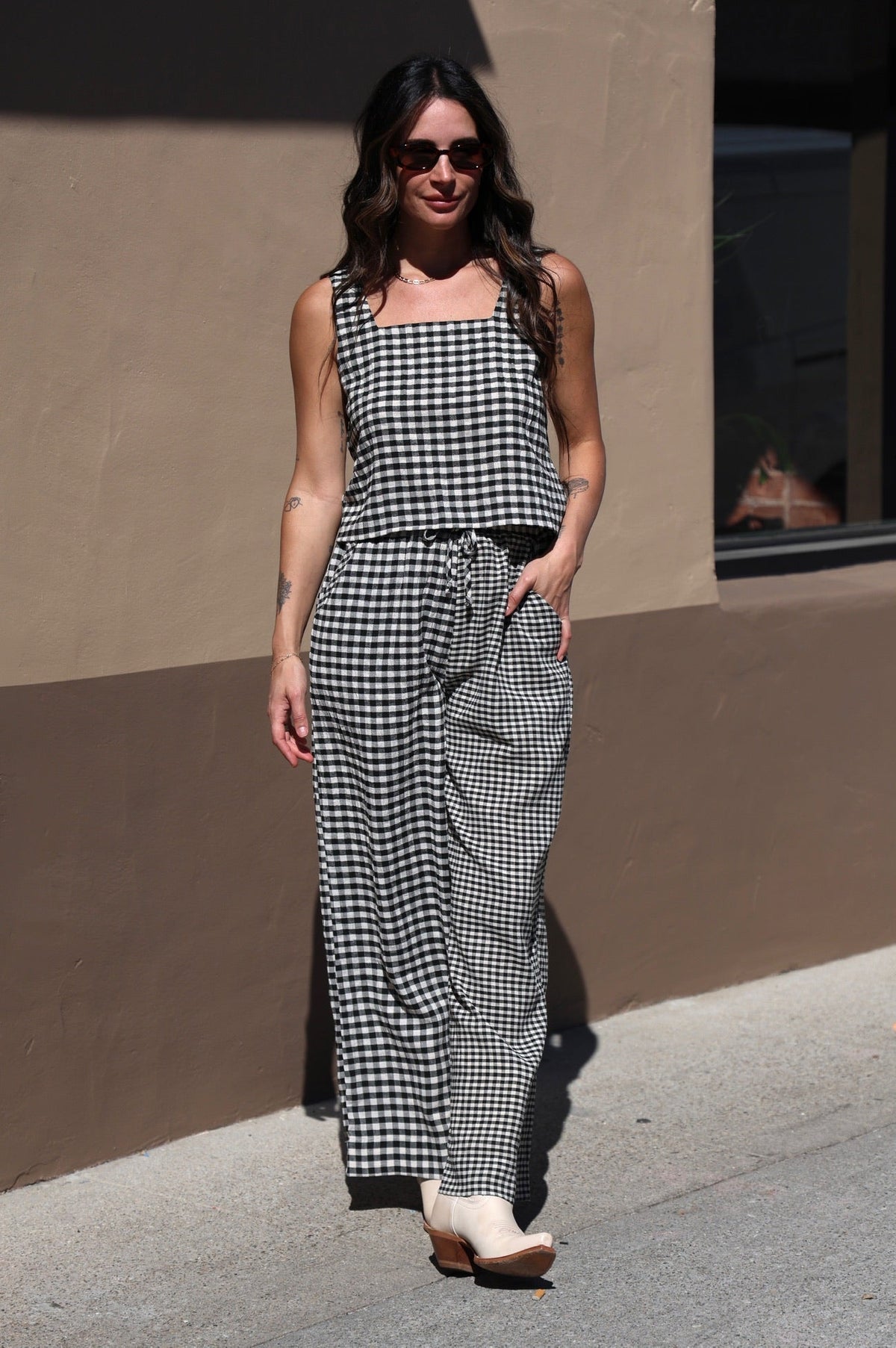 Woman wearing a checkered dress and sunglasses standing on a sidewalk.