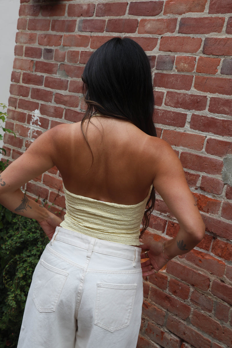 Person wearing a strapless top and white pants against a brick wall