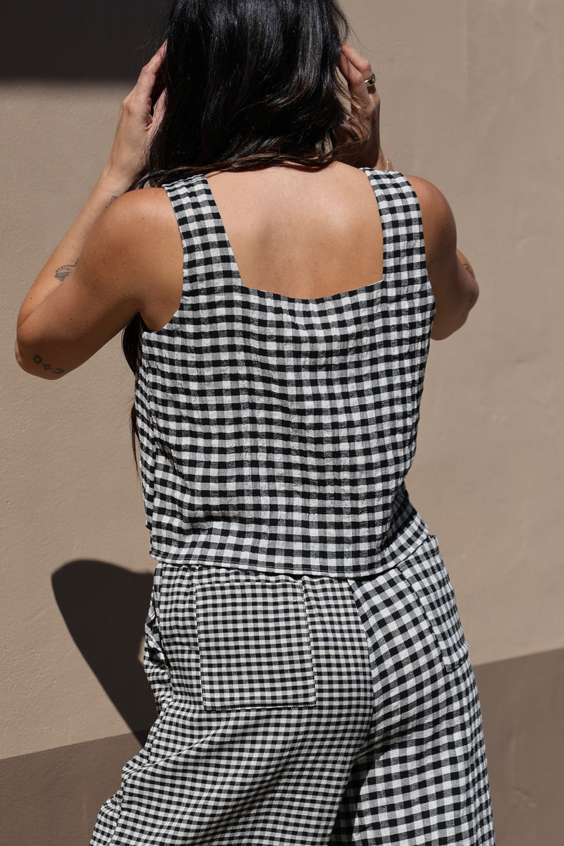 Person wearing a black and white checkered jumpsuit against a beige wall.