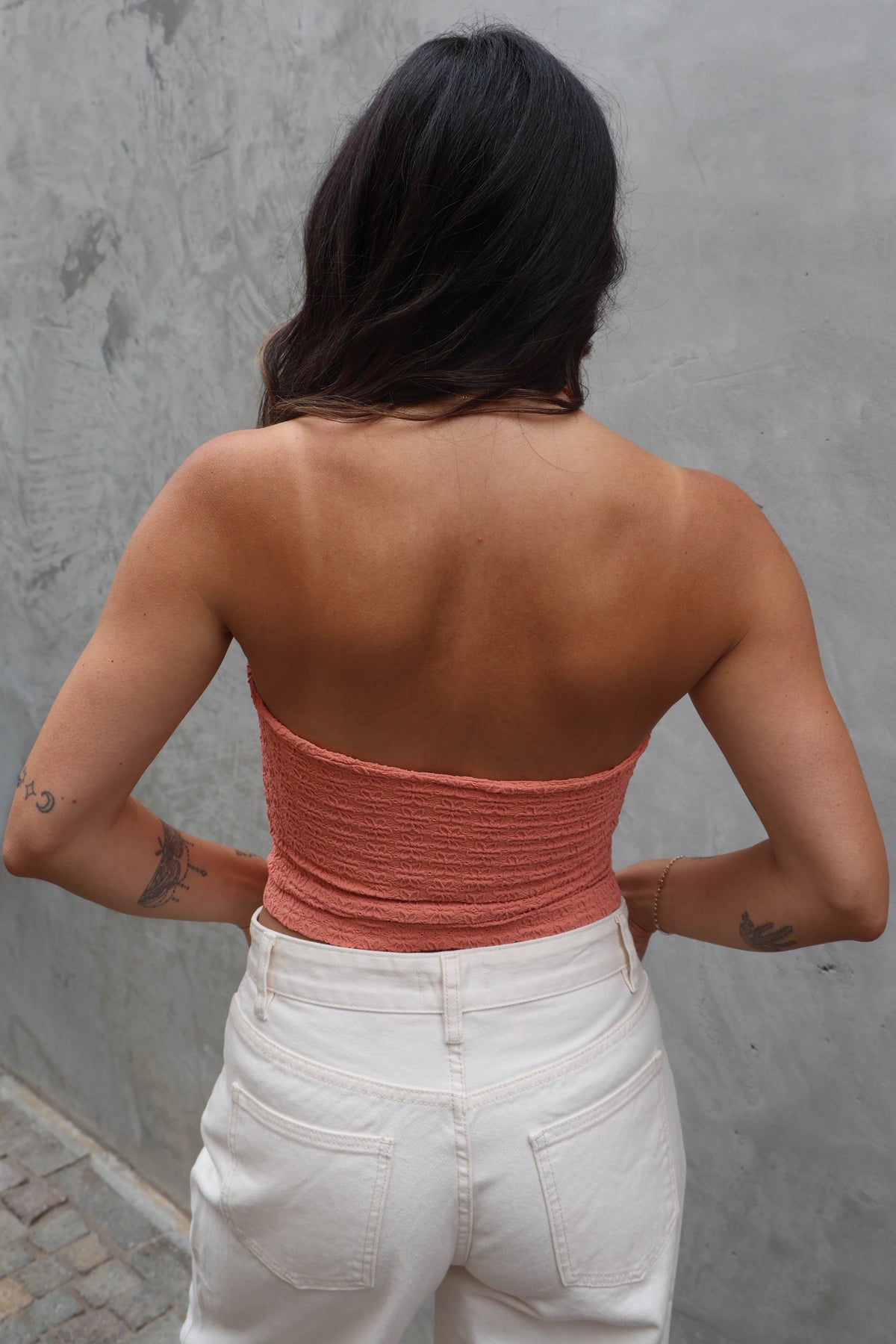 Person wearing a pink top and white pants against a gray wall