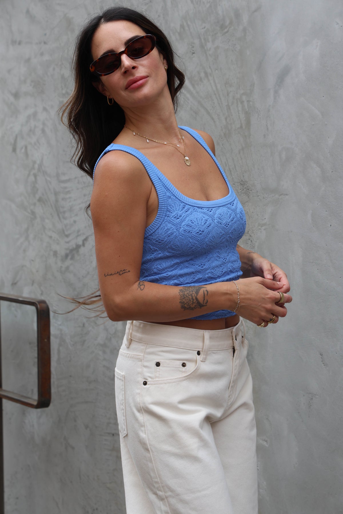 Woman wearing a blue top and white pants against a gray wall