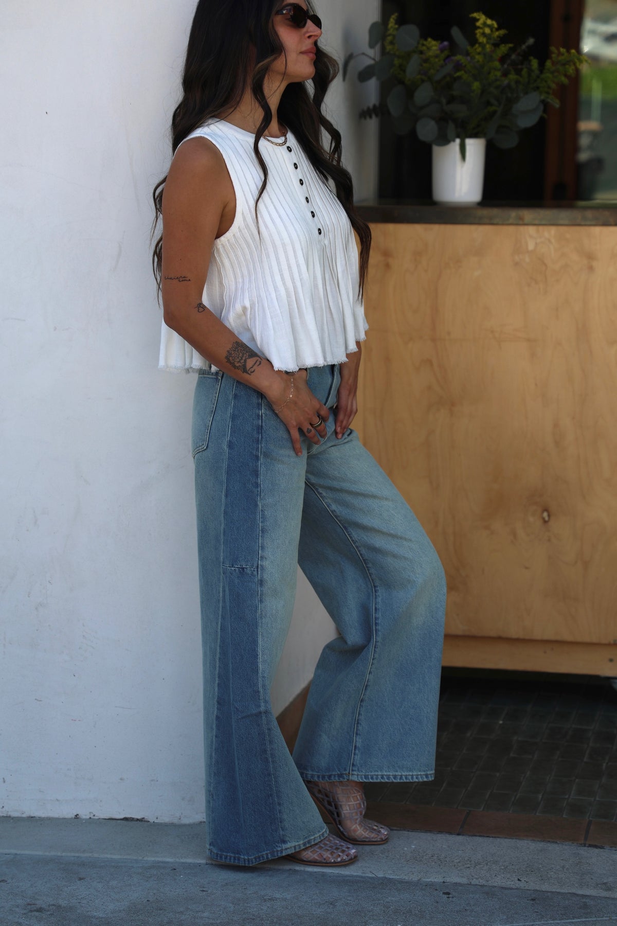 Woman wearing a white blouse and blue jeans standing against a white wall.