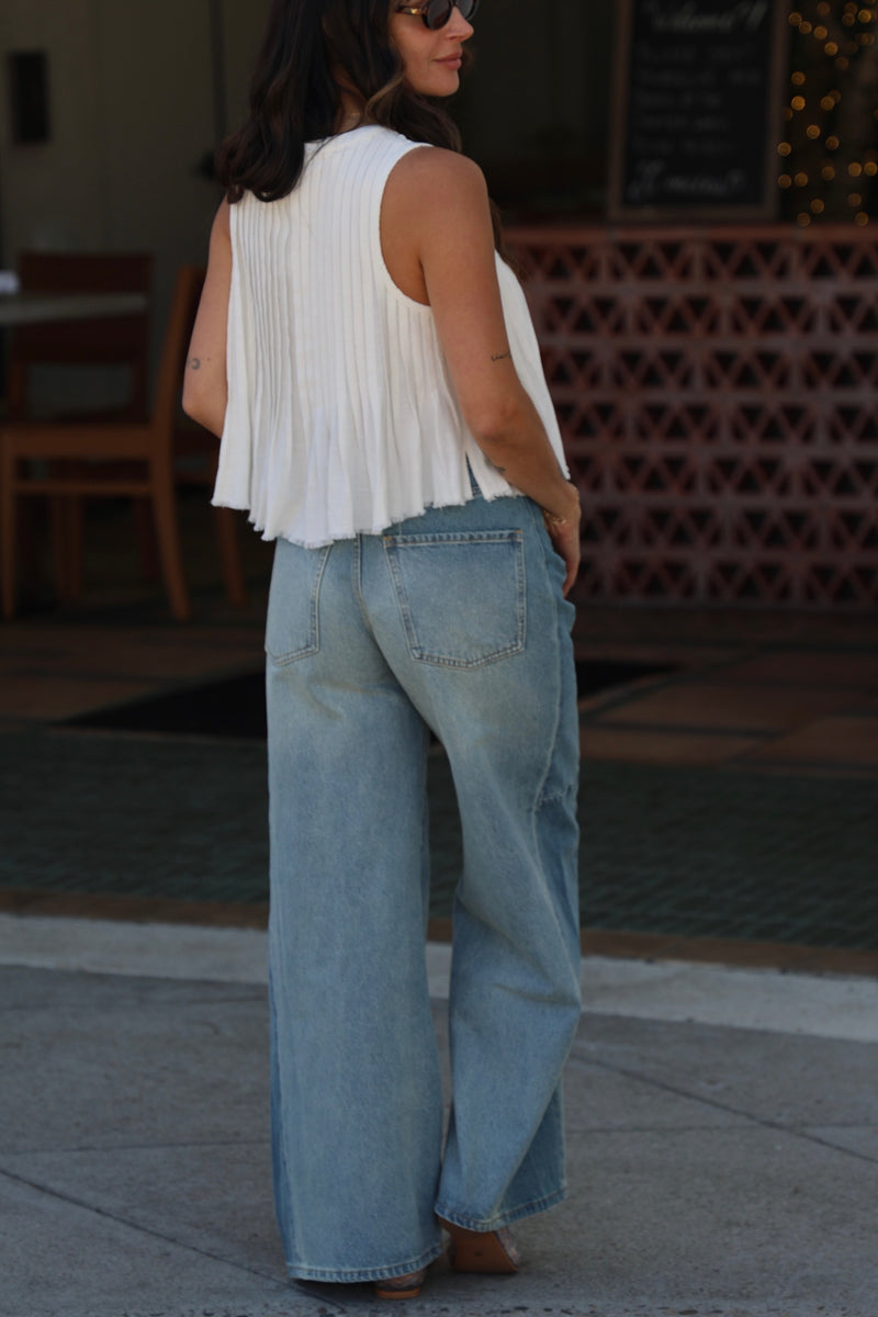 Person wearing a white sleeveless top and blue jeans walking outdoors.