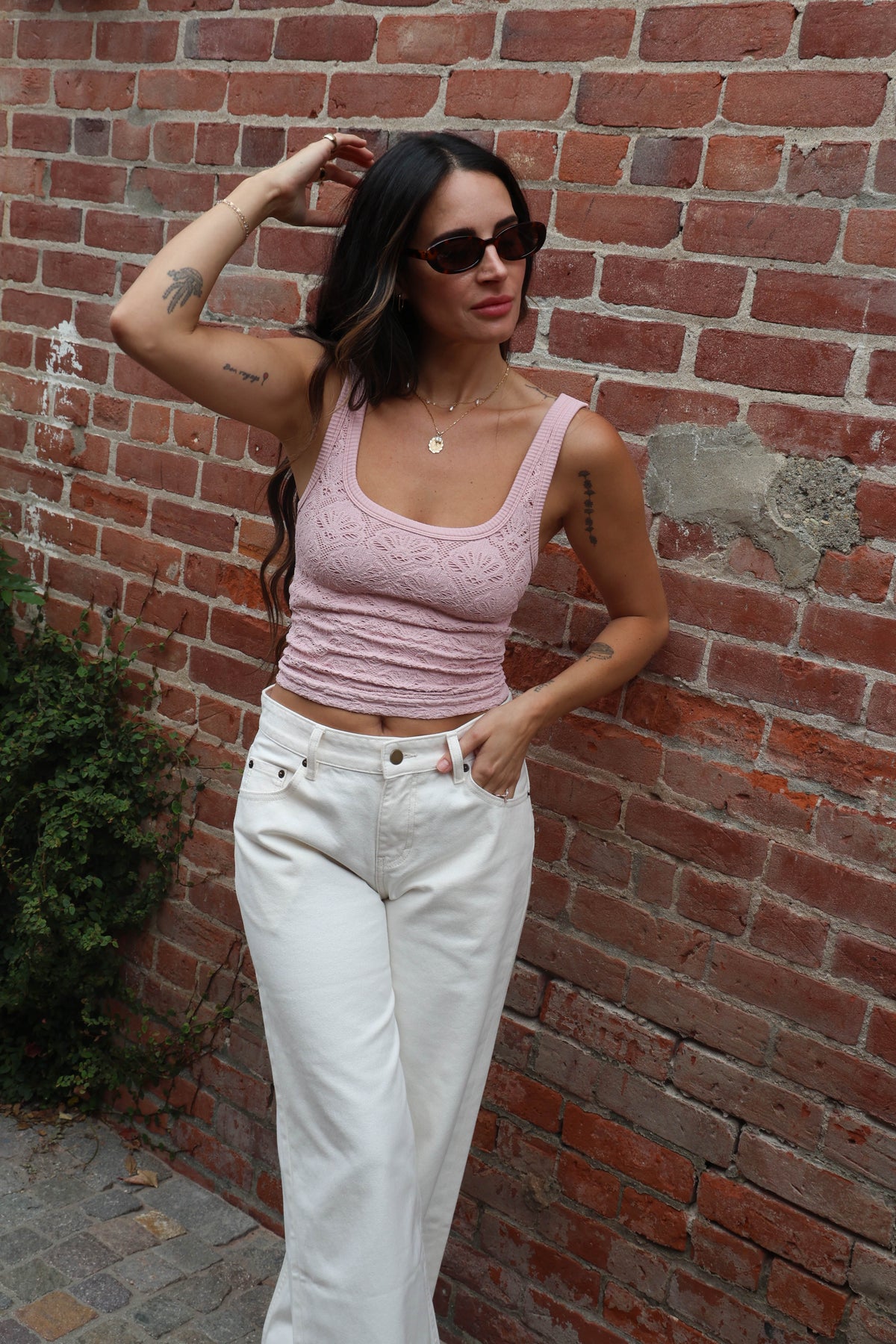 Woman wearing a pink top and white pants against a brick wall