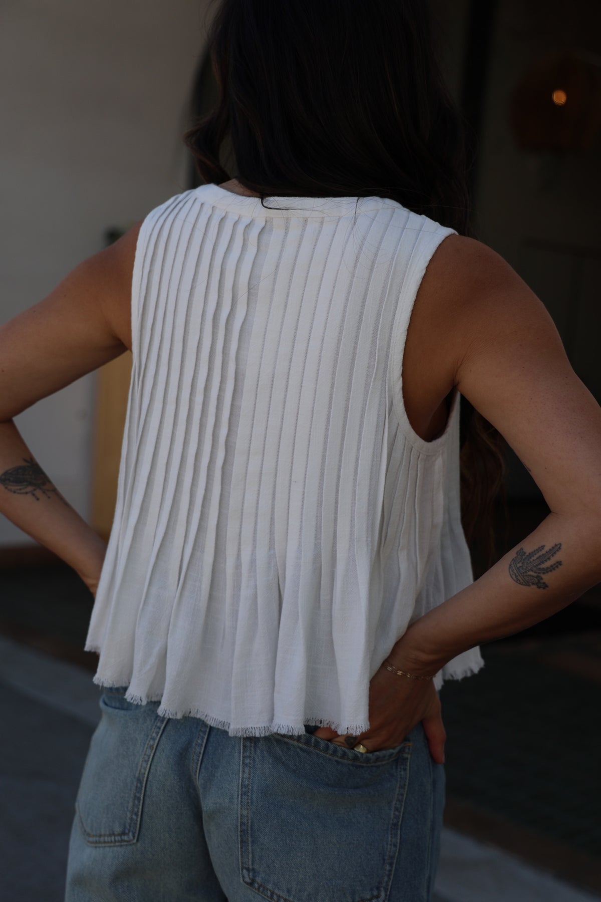 Person wearing a white pleated top and blue jeans with a blurred background