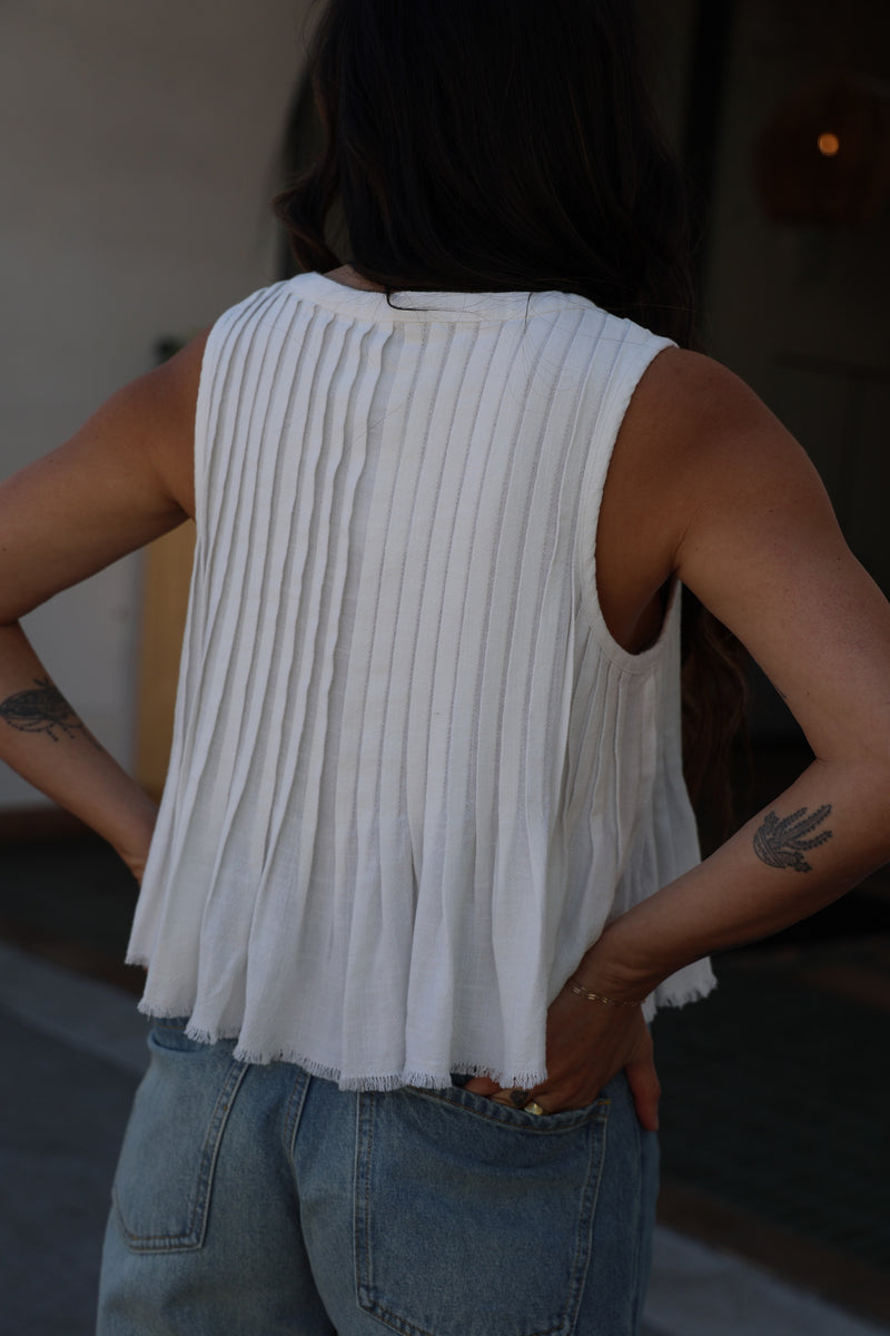 Person wearing a white pleated top and blue jeans with a blurred background